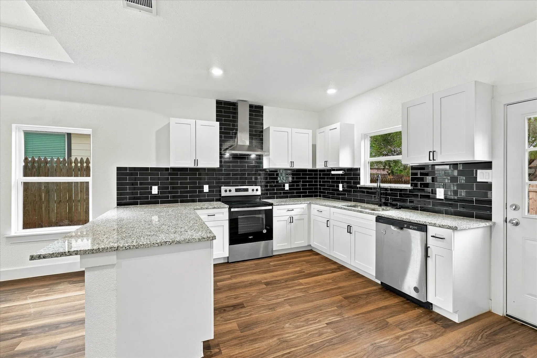 Kitchen featuring white cabinetry, granite countertops, stainless steel appliances, a black subway tile backsplash, and wood-finish flooring
