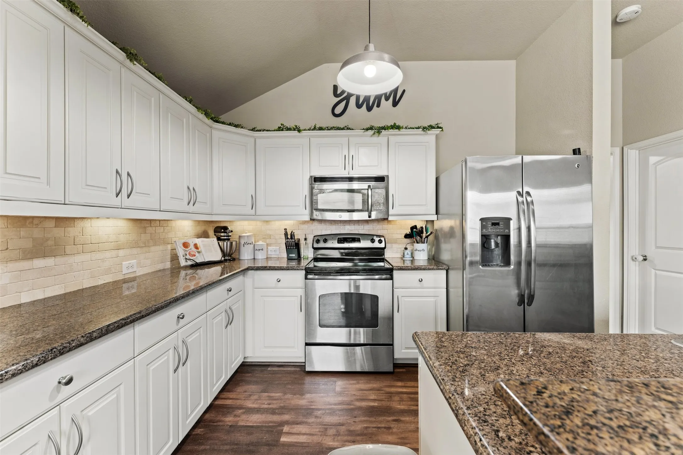 Kitchen featuring white cabinetry, wood-finish flooring, granite countertops, tile backsplash, and stainless steel appliances