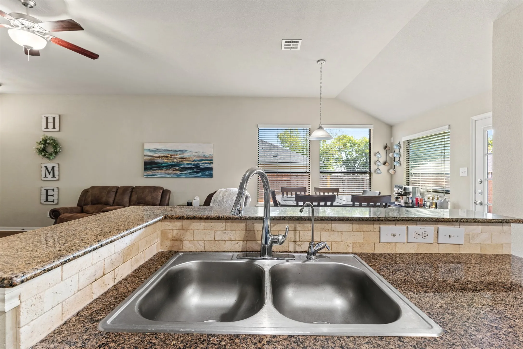 Double-basin stainless steel sink with a chrome faucet, set into a speckled countertop with a tiled backsplash