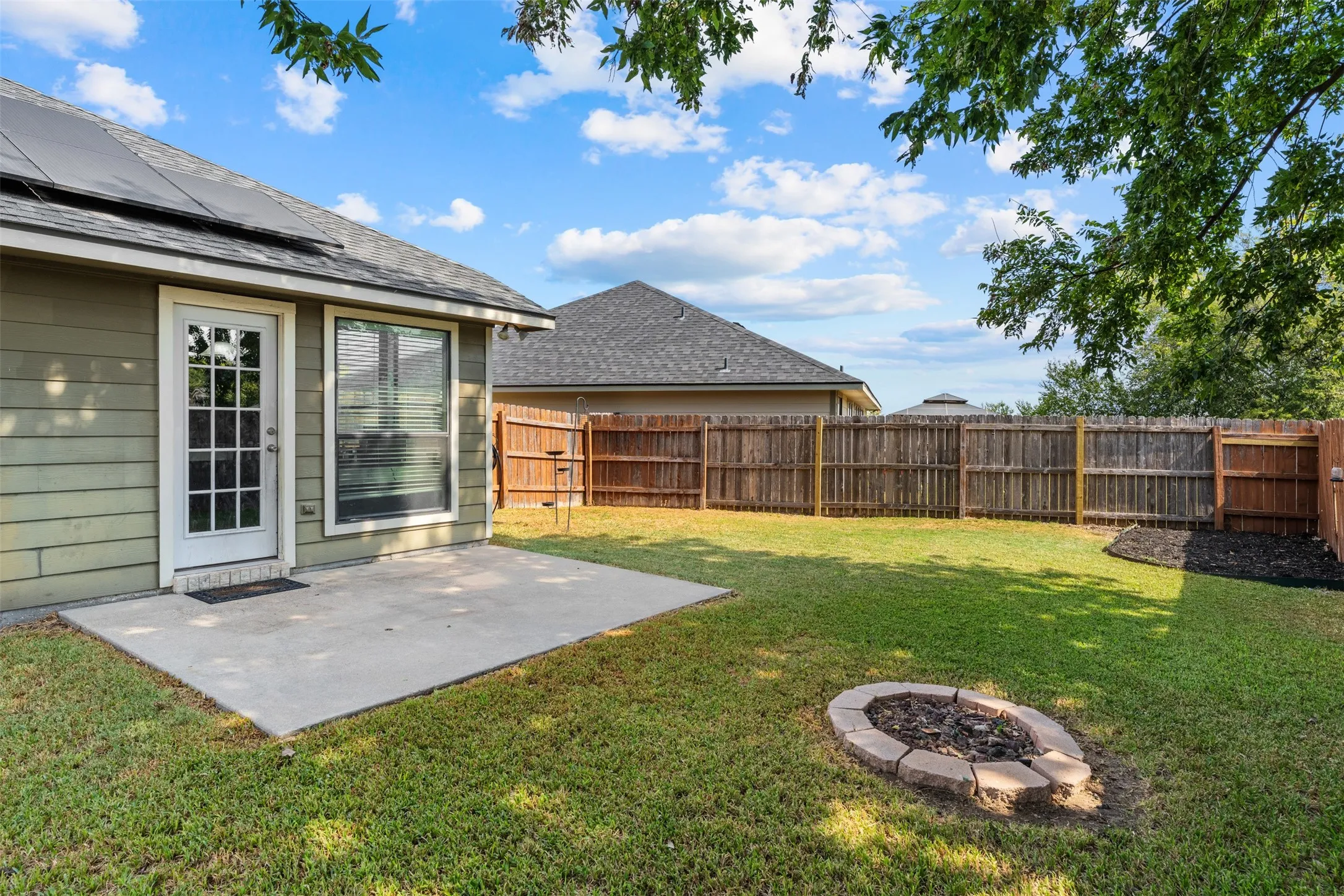 Expansive backyard featuring a concrete patio, a built-in fire pit, and wood privacy fencing