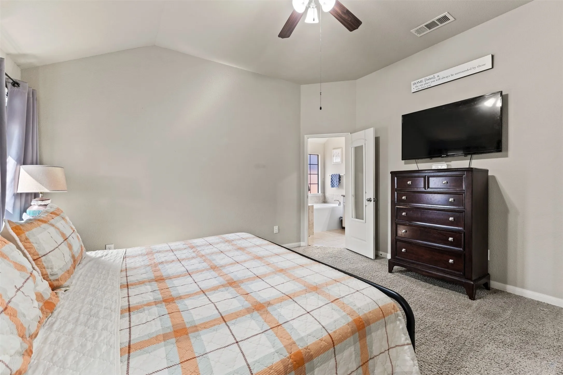 Vaulted ceiling with a ceiling fan, carpeted flooring, and an en-suite bathroom access with a soaking tub