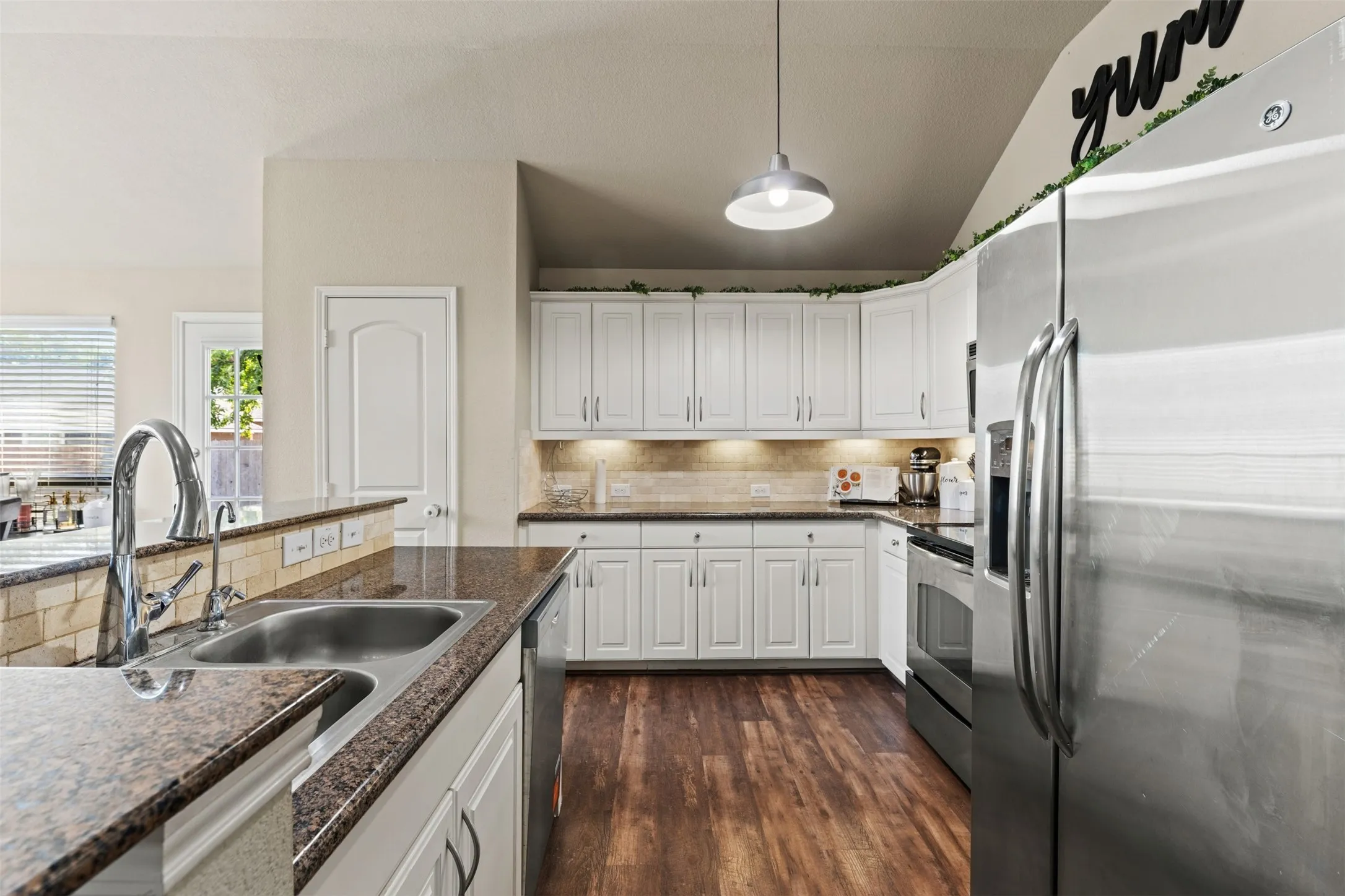 Well-appointed kitchen featuring white cabinetry, wood-finish flooring, stainless steel appliances, granite-look countertops, and an undermount sink