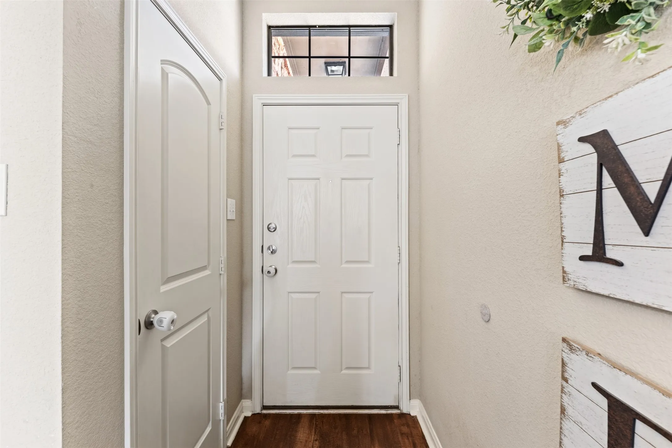 Wood-finish flooring, white paneled door, and a transom window above the entry door