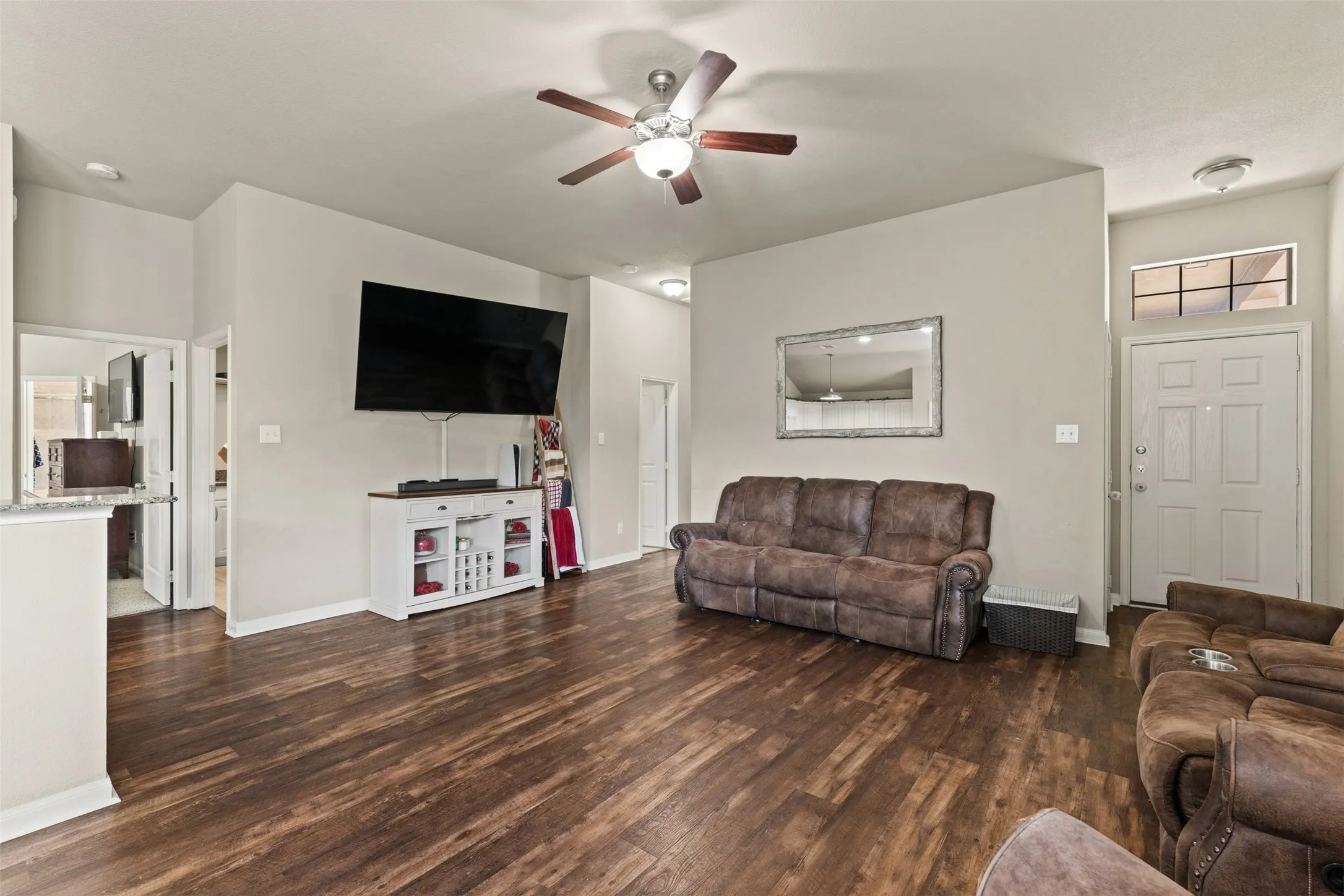 Wood-finish flooring throughout, ceiling fan with integrated lighting, and a front entry door with transom window
