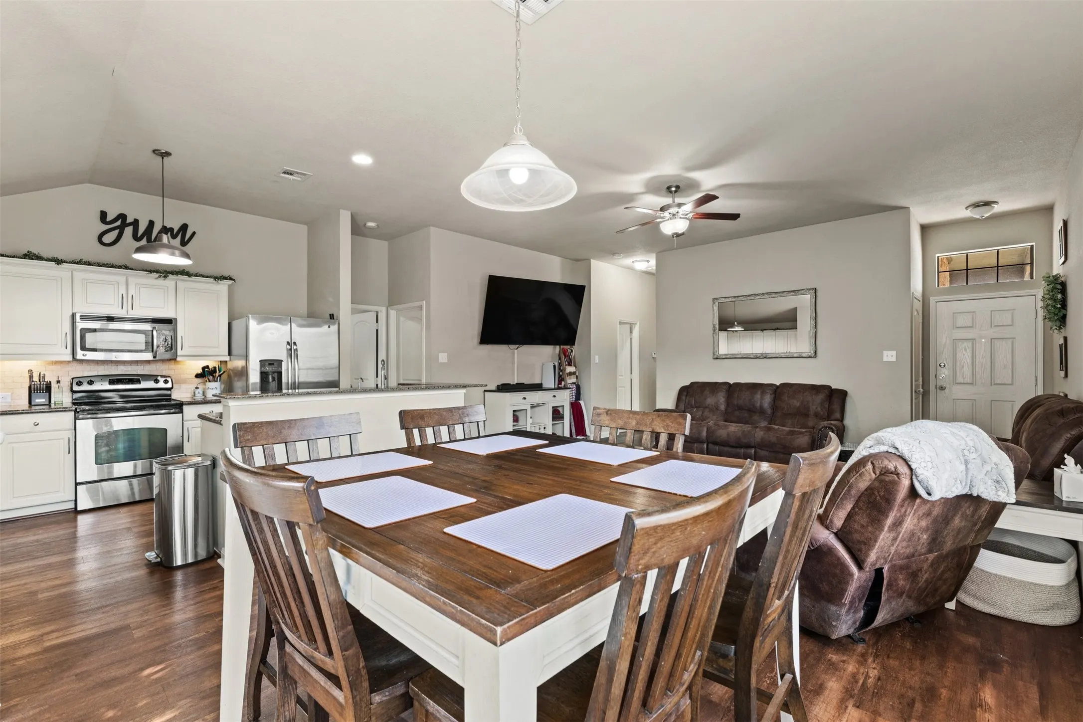 Open-concept living space with wood-finish flooring, a kitchen featuring white cabinetry and stainless steel appliances, and a dining area with a wood-top table