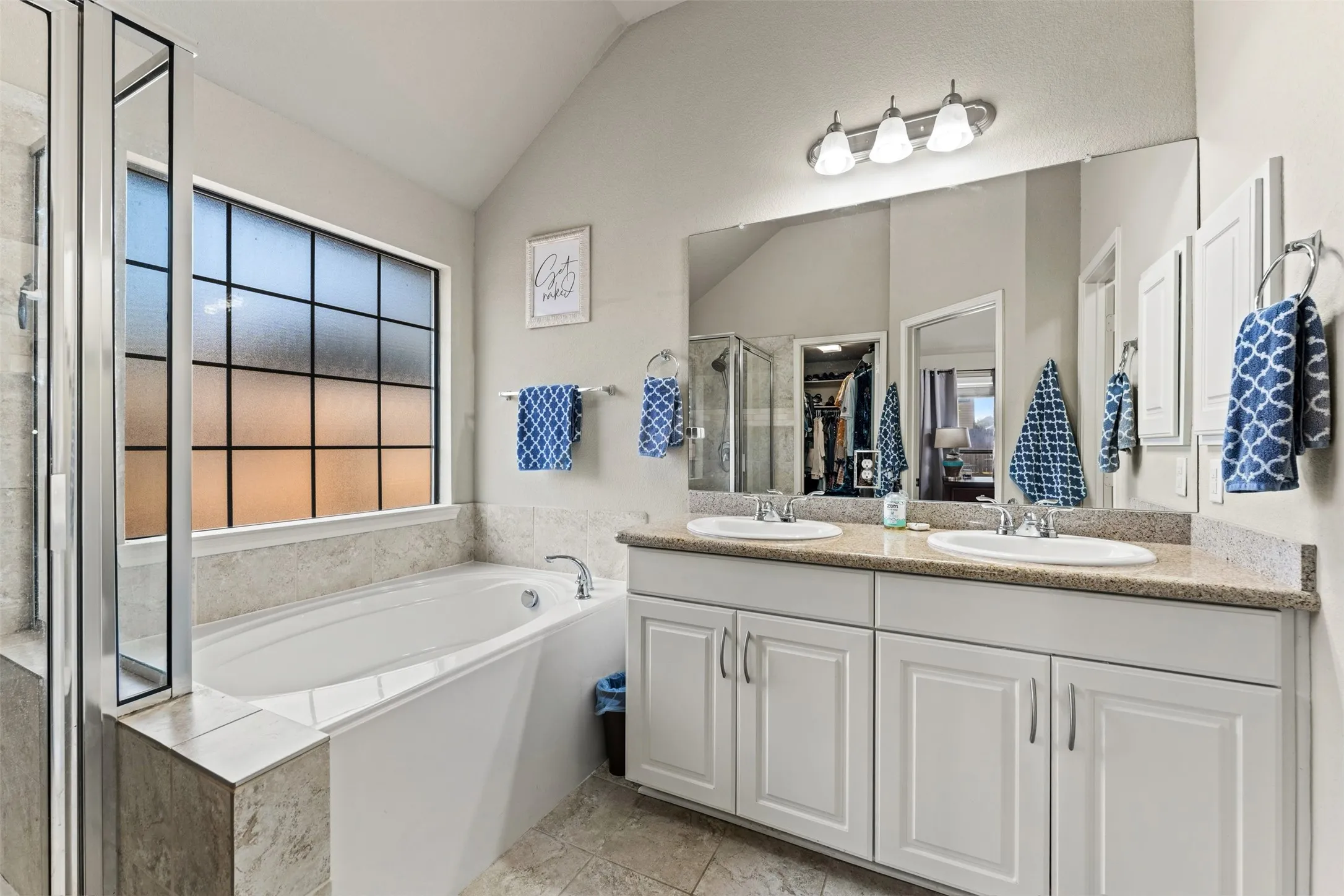 Dual vanity with undermount sinks, spacious bathtub, separate shower enclosure with glass panels, and a large privacy window