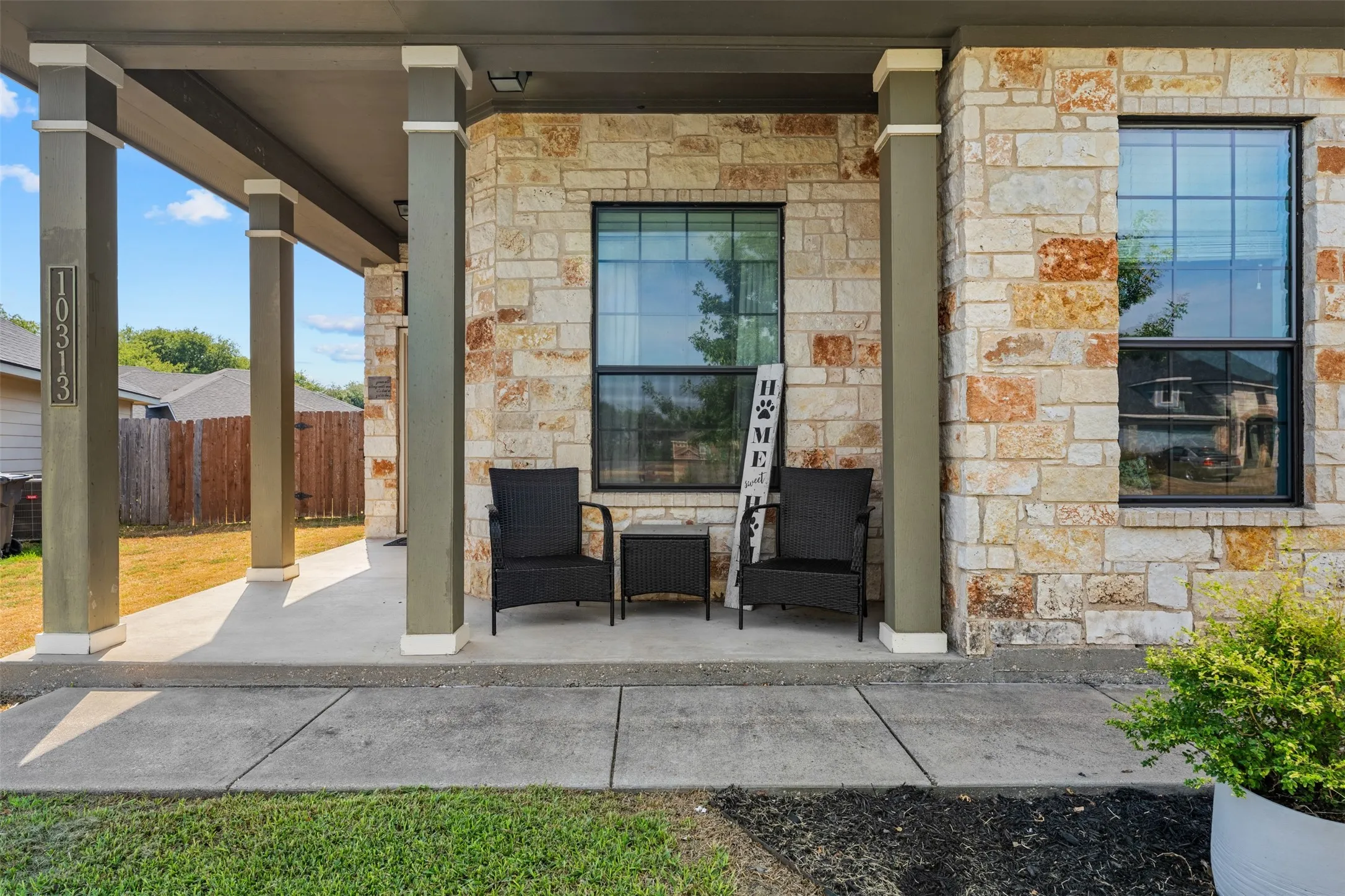 Limestone and brick veneer exterior with a covered concrete porch, multiple square columns, and dark-framed windows
