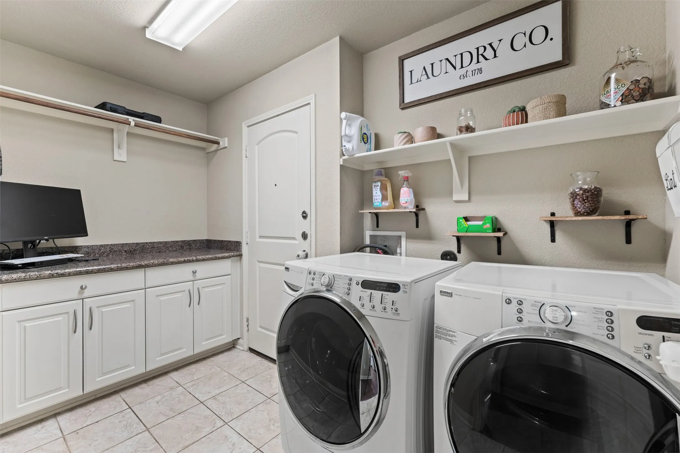 White cabinetry with dark speckled countertops, tiled flooring, and multiple wall-mounted shelves