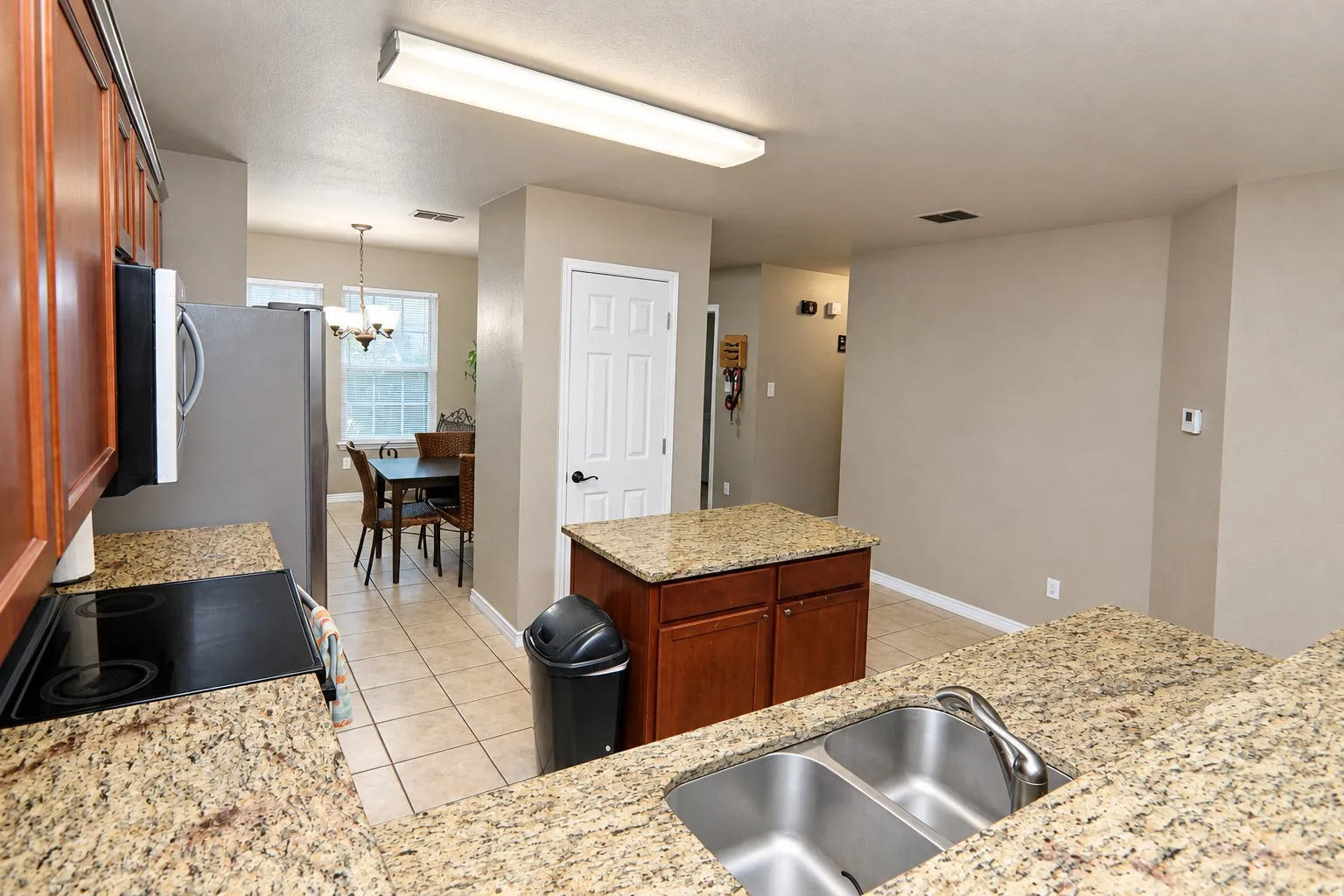 Kitchen featuring granite countertops, wood cabinetry, stainless steel sink, and tile flooring