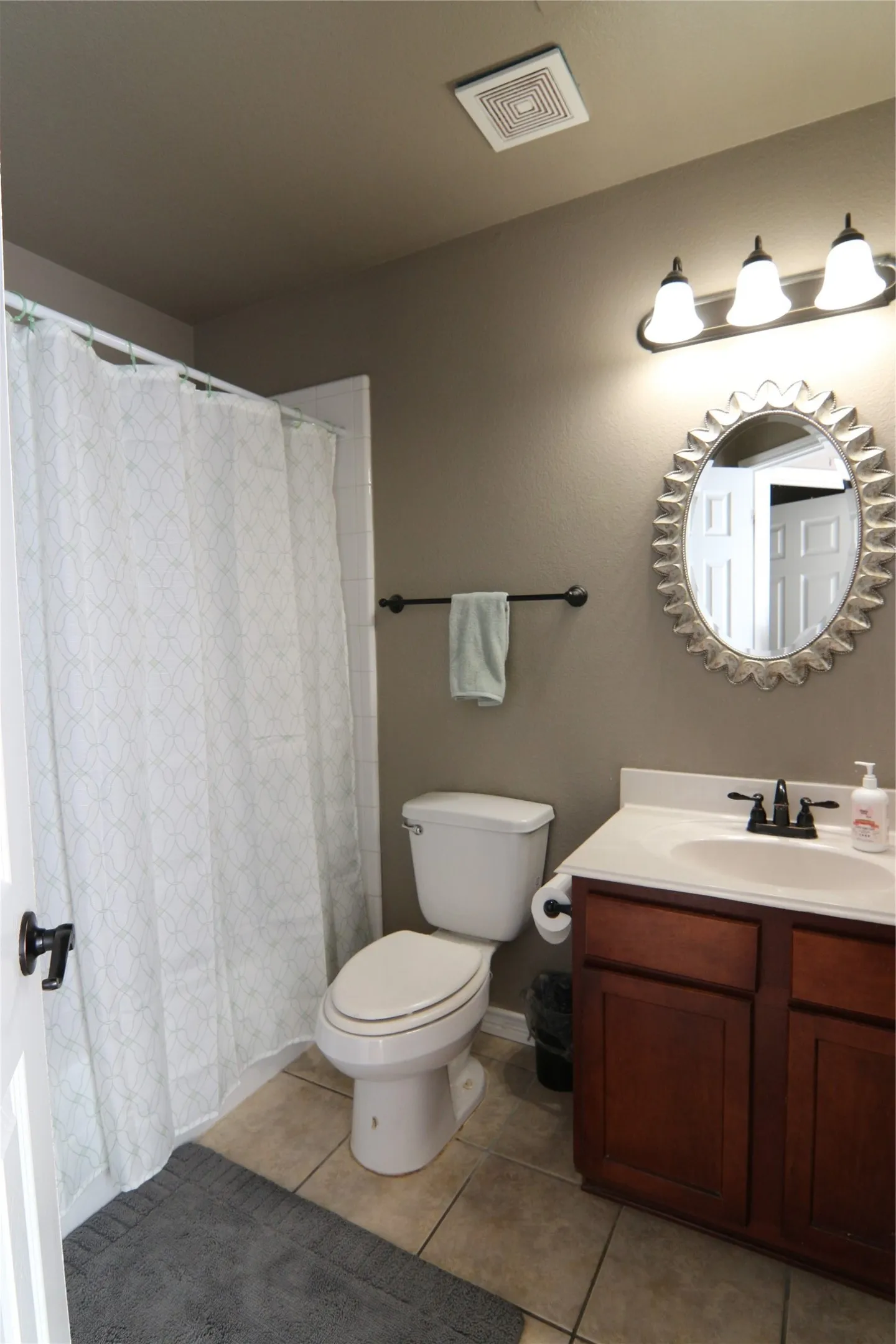Tiled flooring, single vanity with wood-finish cabinetry and integrated sink, wall-mounted light fixture, and a toilet
