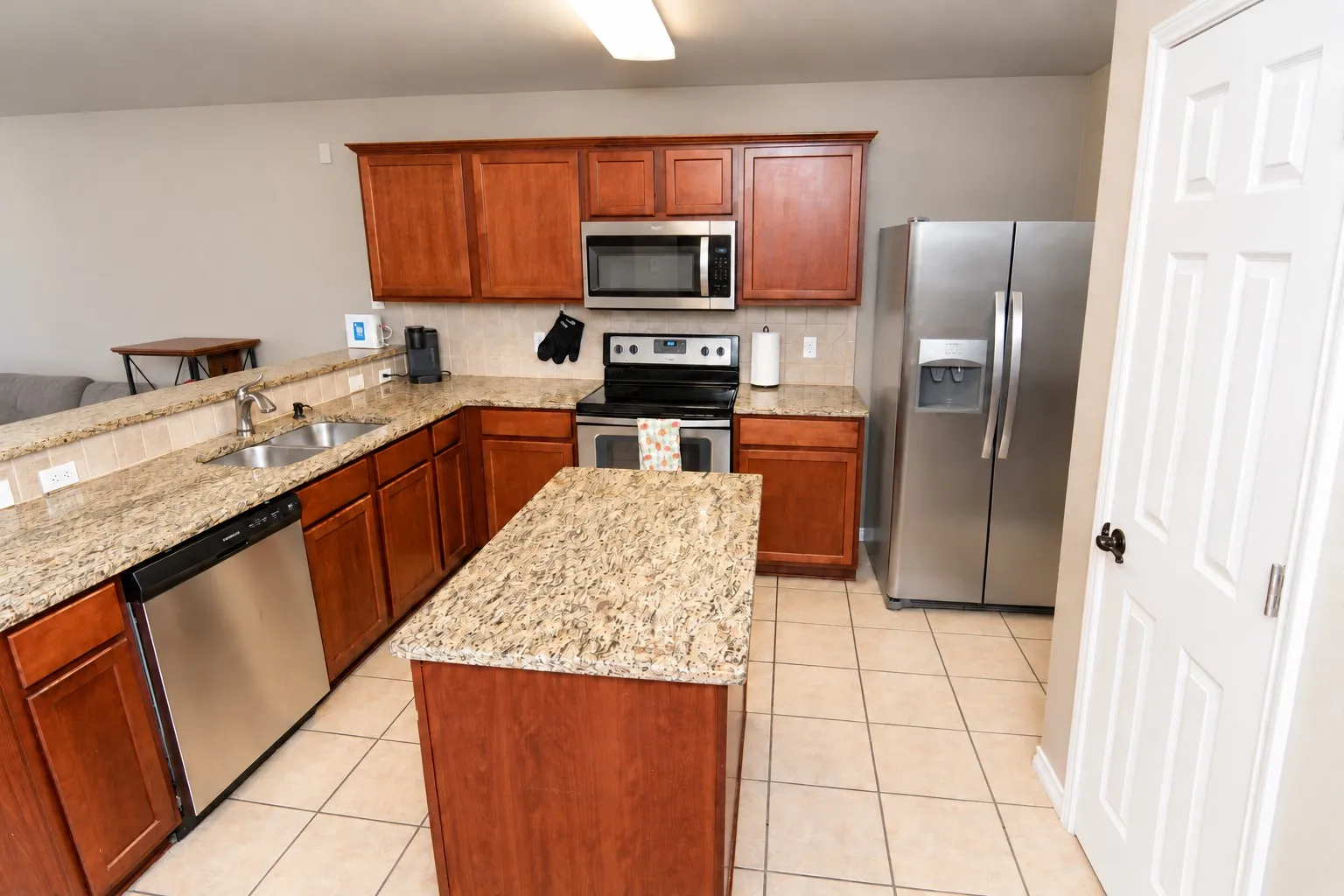 Kitchen featuring wood cabinetry, light-toned countertops, a stainless steel double sink, and tile flooring