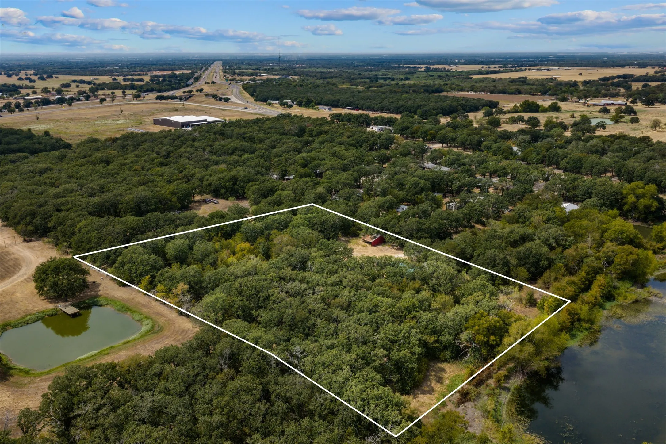 Wooded acreage featuring a red structure and a water body along the property perimeter