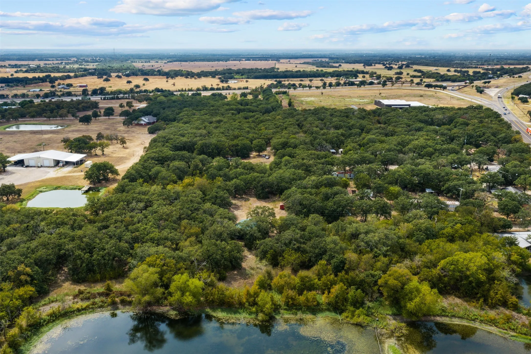 Expansive property featuring mature tree coverage, multiple water features, and a large metal outbuilding