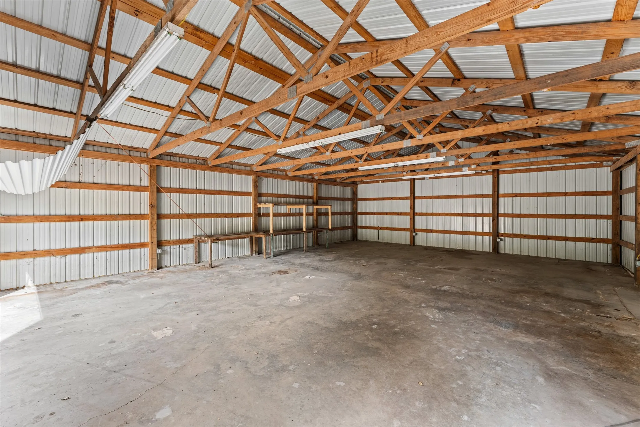 Concrete flooring, exposed wood beam ceiling, corrugated metal walls, built-in shelving, and overhead fluorescent lighting