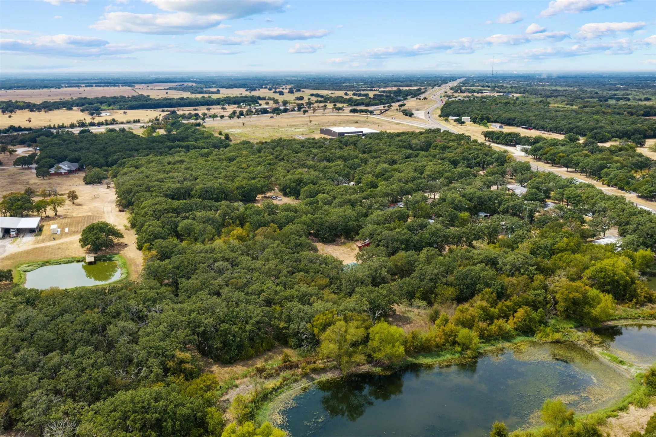 Expansive land parcel featuring dense tree coverage, multiple water features, and a distant highway access