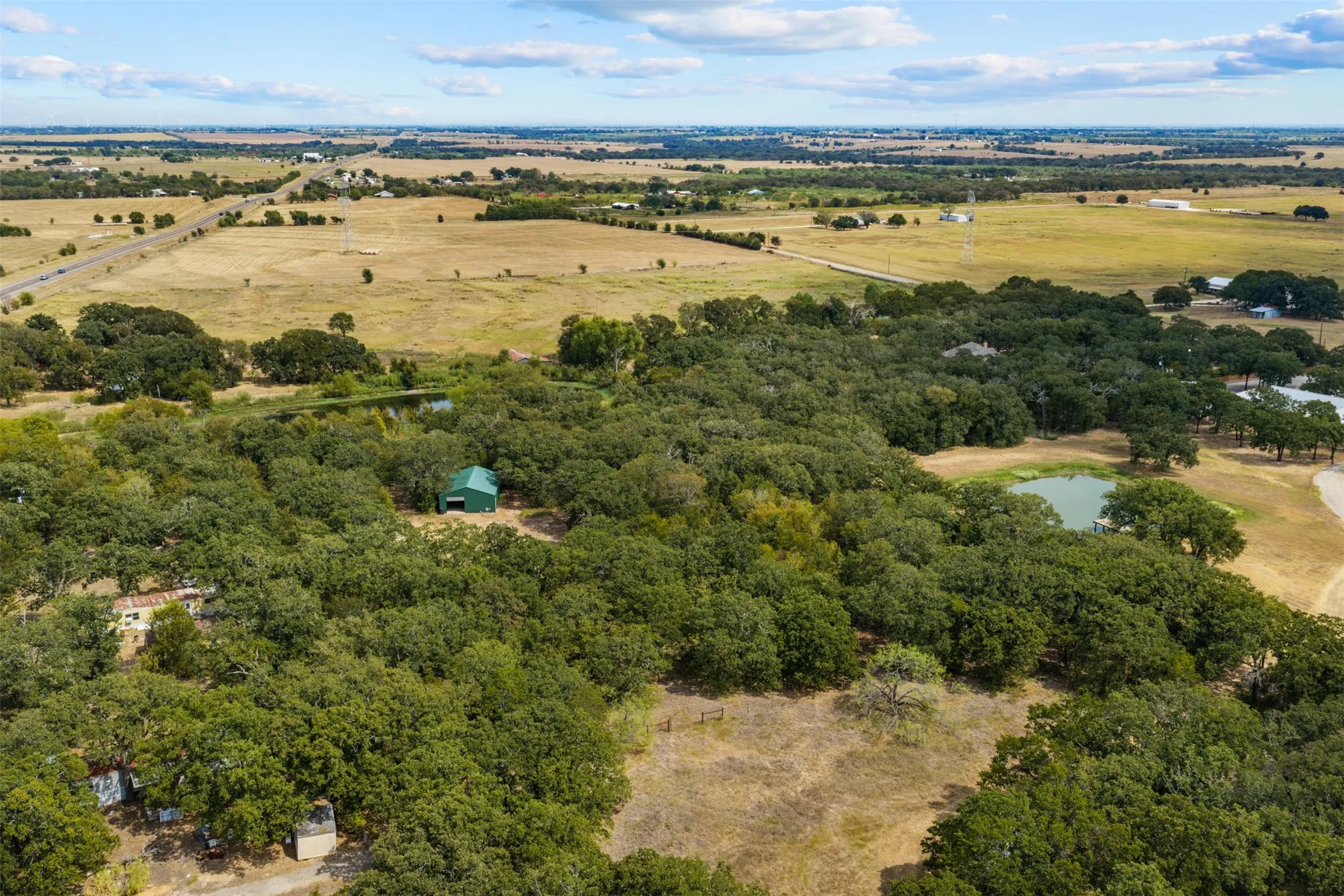 Expansive land featuring significant tree coverage, a natural pond, and a green outbuilding