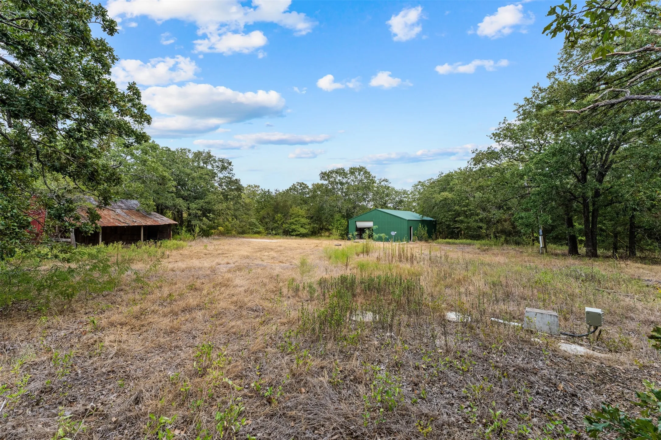 Expansive open field with scattered trees, featuring a red structure with a covered porch and a green metal building