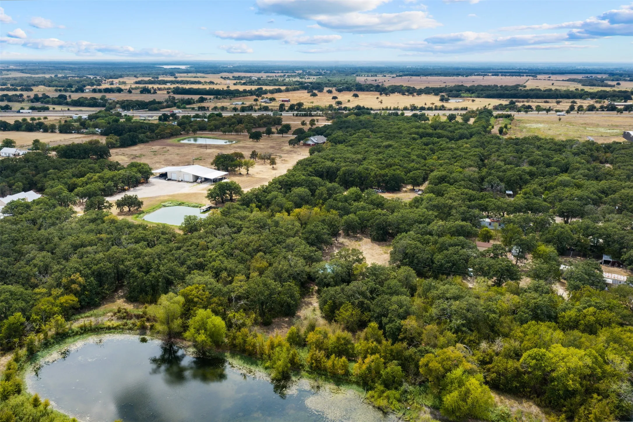 Expansive property featuring dense tree coverage, multiple ponds, and a large outbuilding