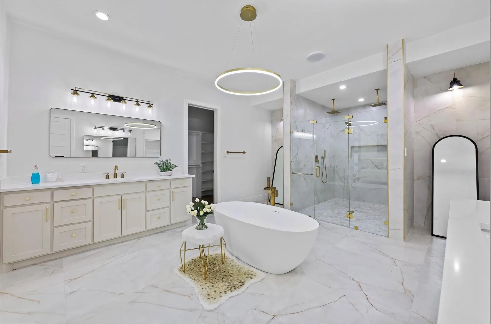 Spacious bathroom featuring a freestanding soaking tub, dual vanity with undermount sinks, glass-enclosed shower with multiple shower heads, and large format marble-look tile flooring