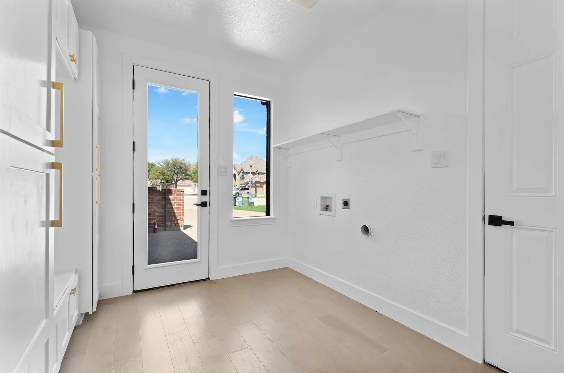 Built-in white cabinetry with gold-tone hardware, wood-finish flooring, full-light door, and a single window