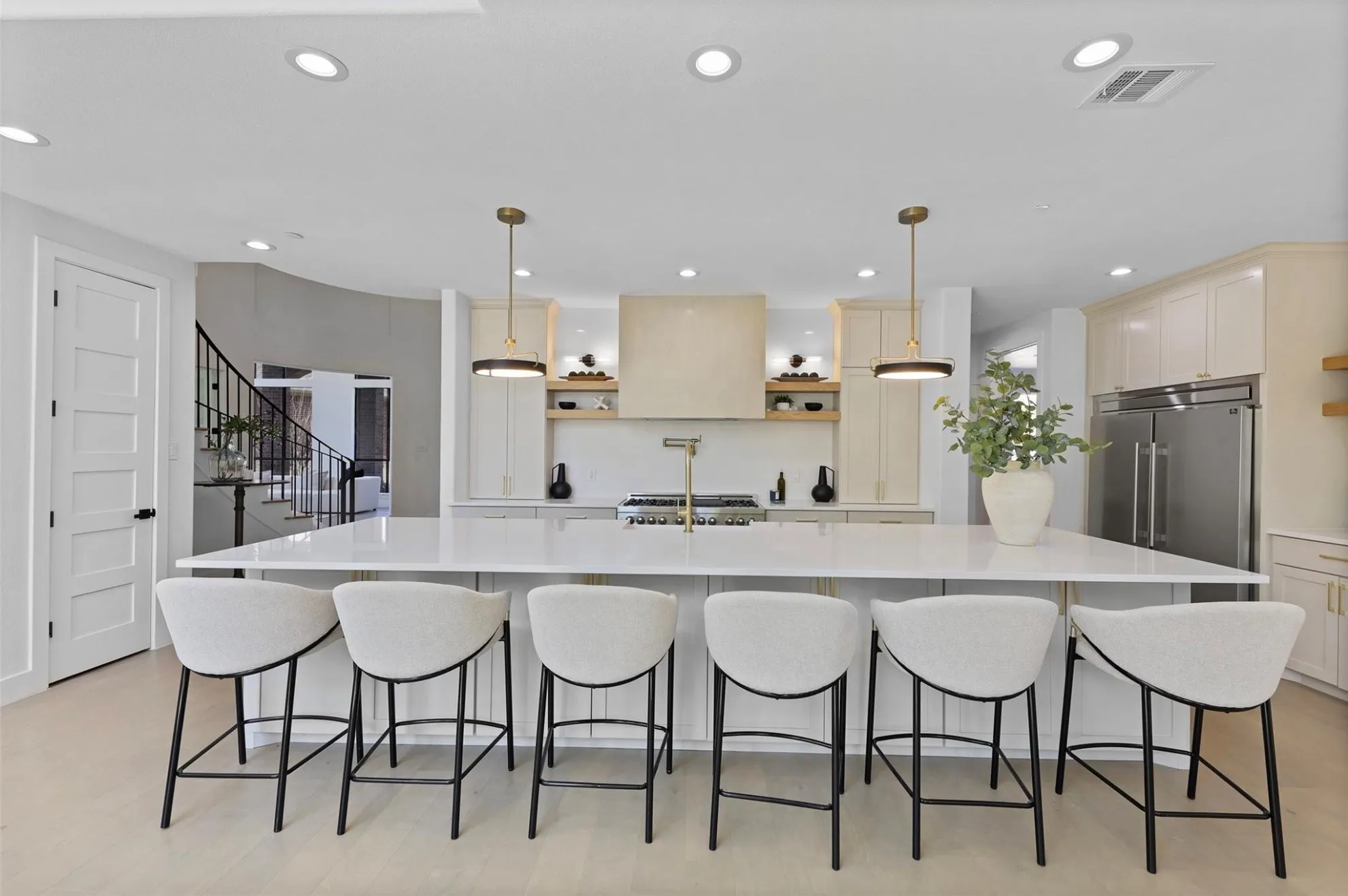Spacious kitchen island with a white countertop, recessed lighting, stainless steel refrigerator, and gold-tone kitchen fixtures
