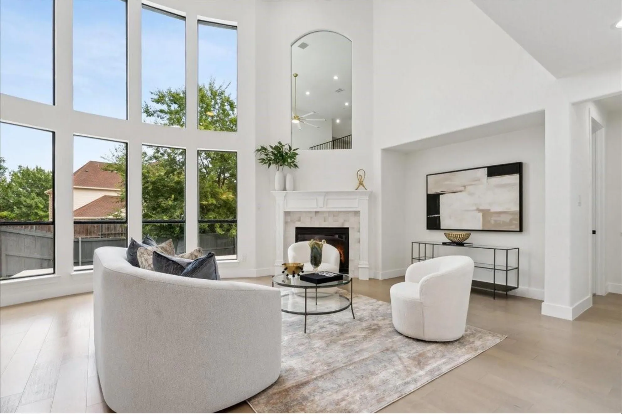 Soaring ceilings, expansive window wall, light wood-finish flooring, fireplace with stone surround, and a white mantel