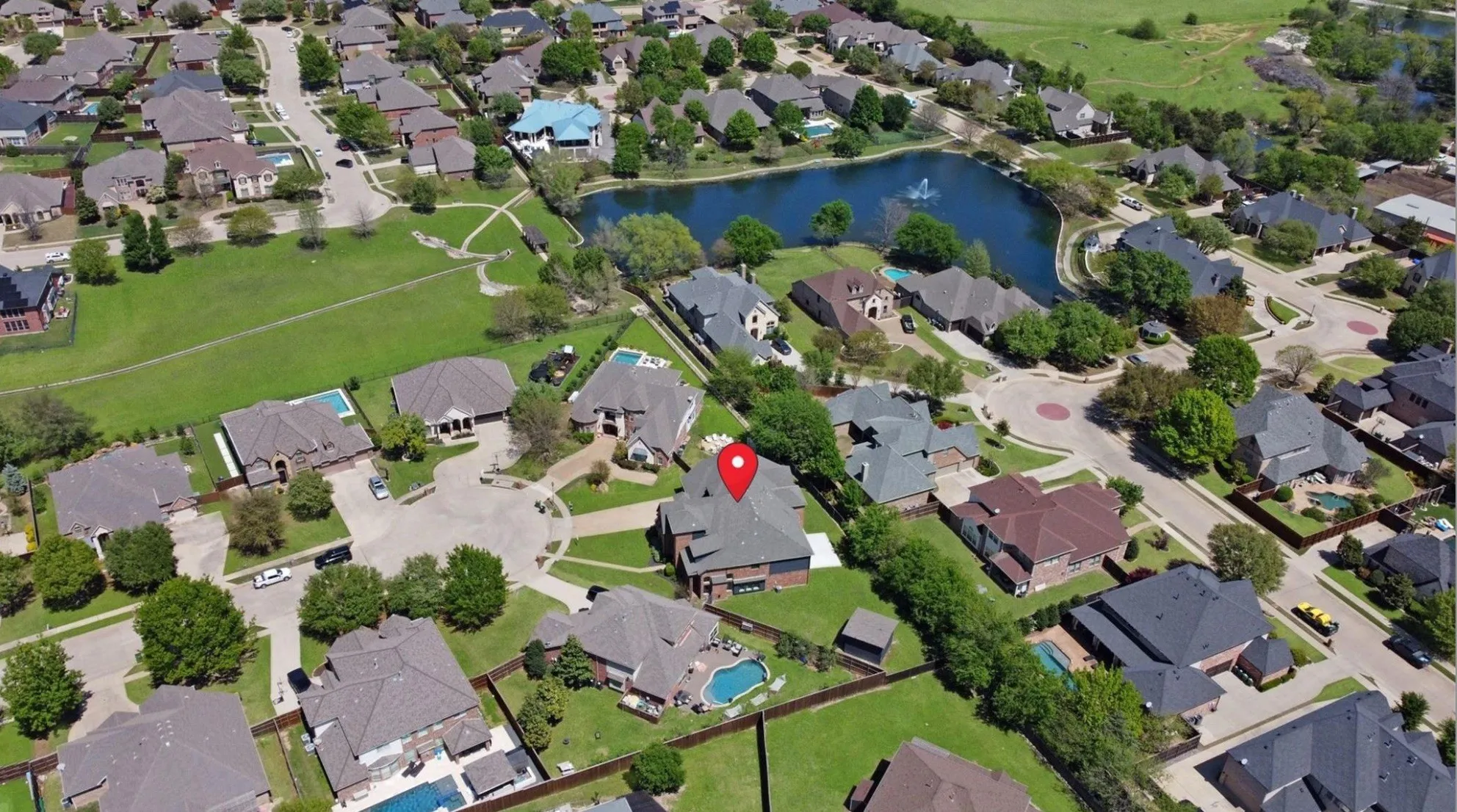 Aerial perspective of a residential neighborhood featuring established homes, mature trees, and a central pond