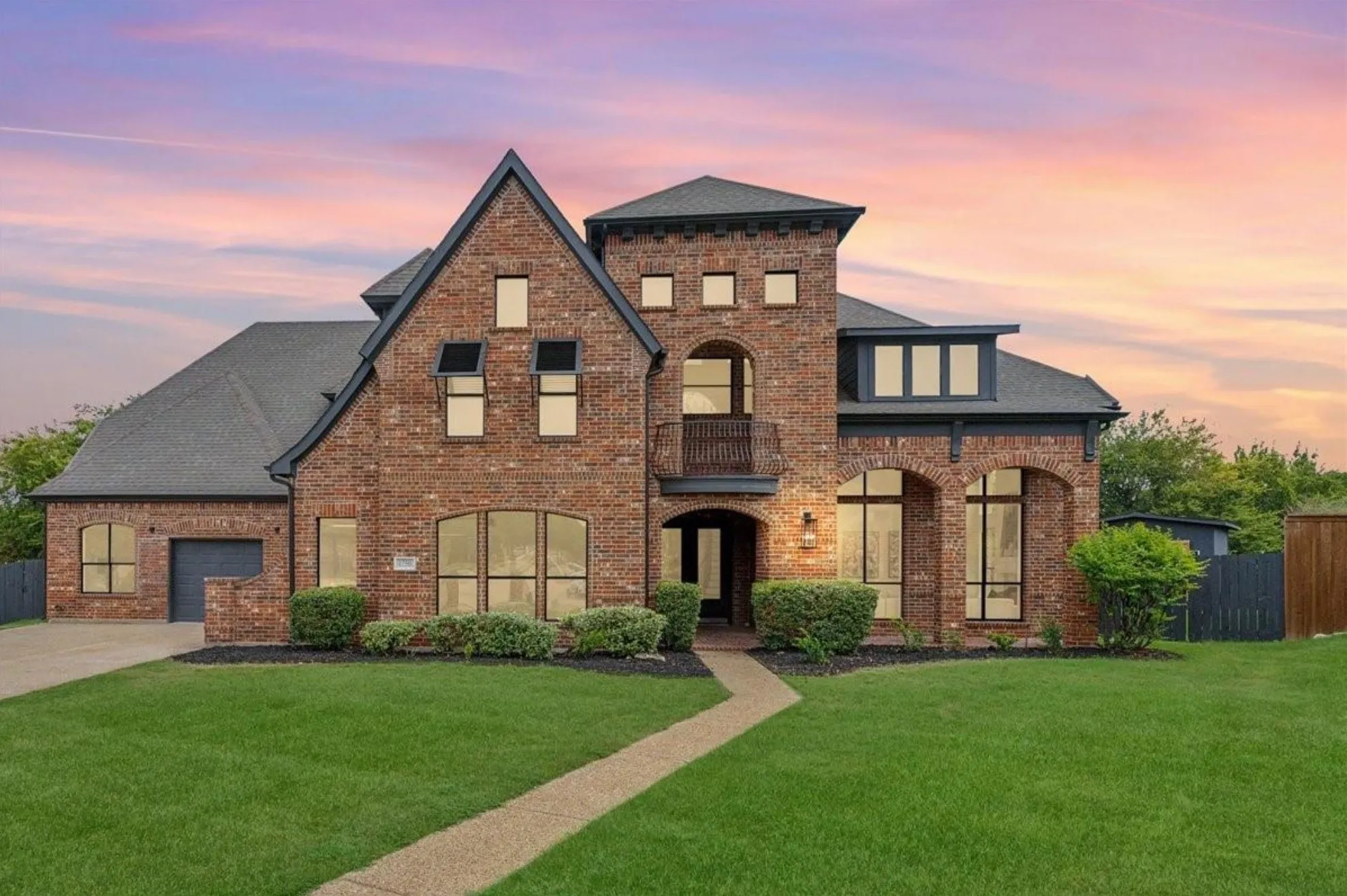 Brick exterior with dark gray roofing, an integrated garage, a second-story balcony, and arched window details