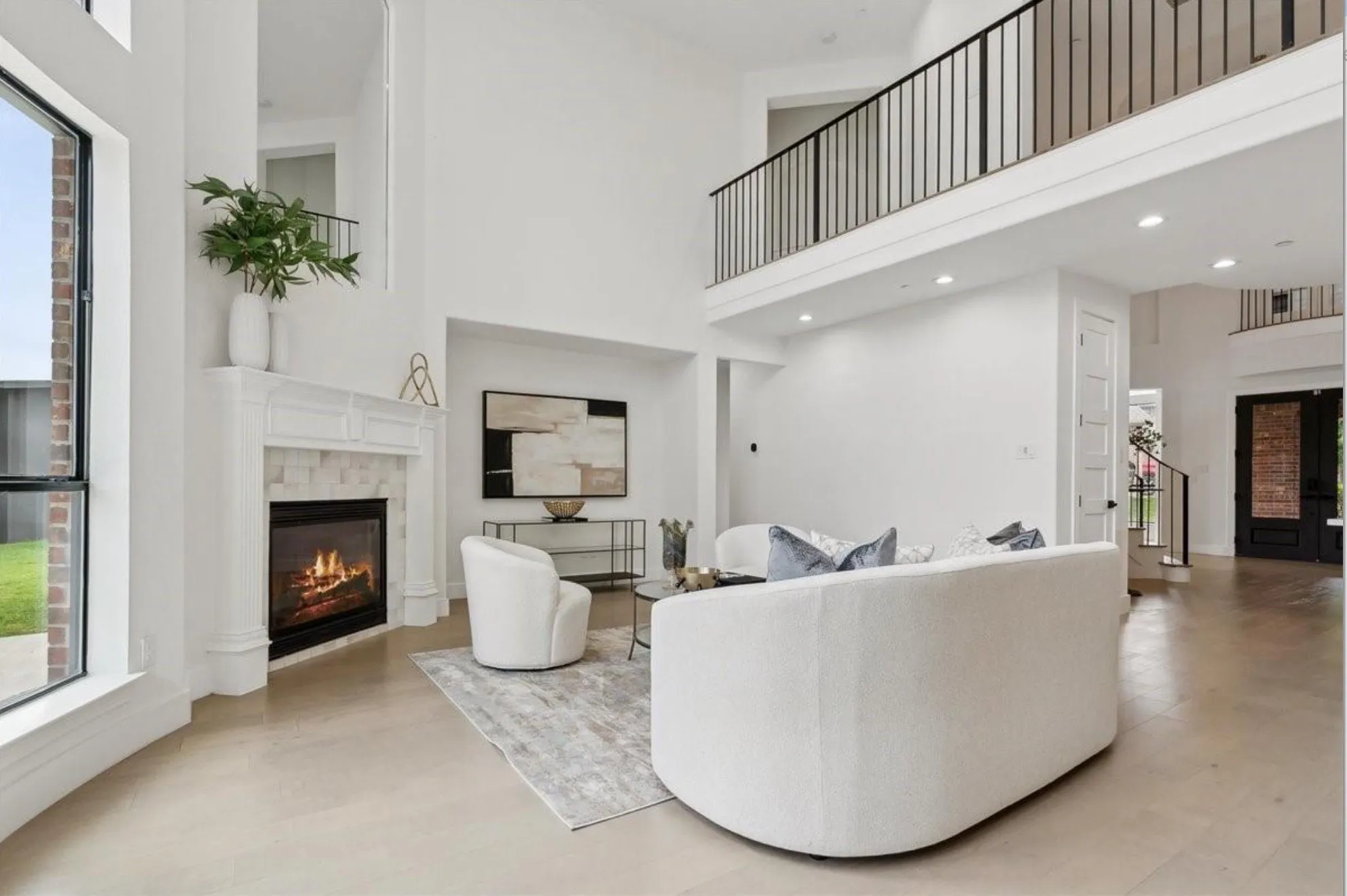 Two-story living area with high ceilings, featuring a gas fireplace with a white mantel and tile surround