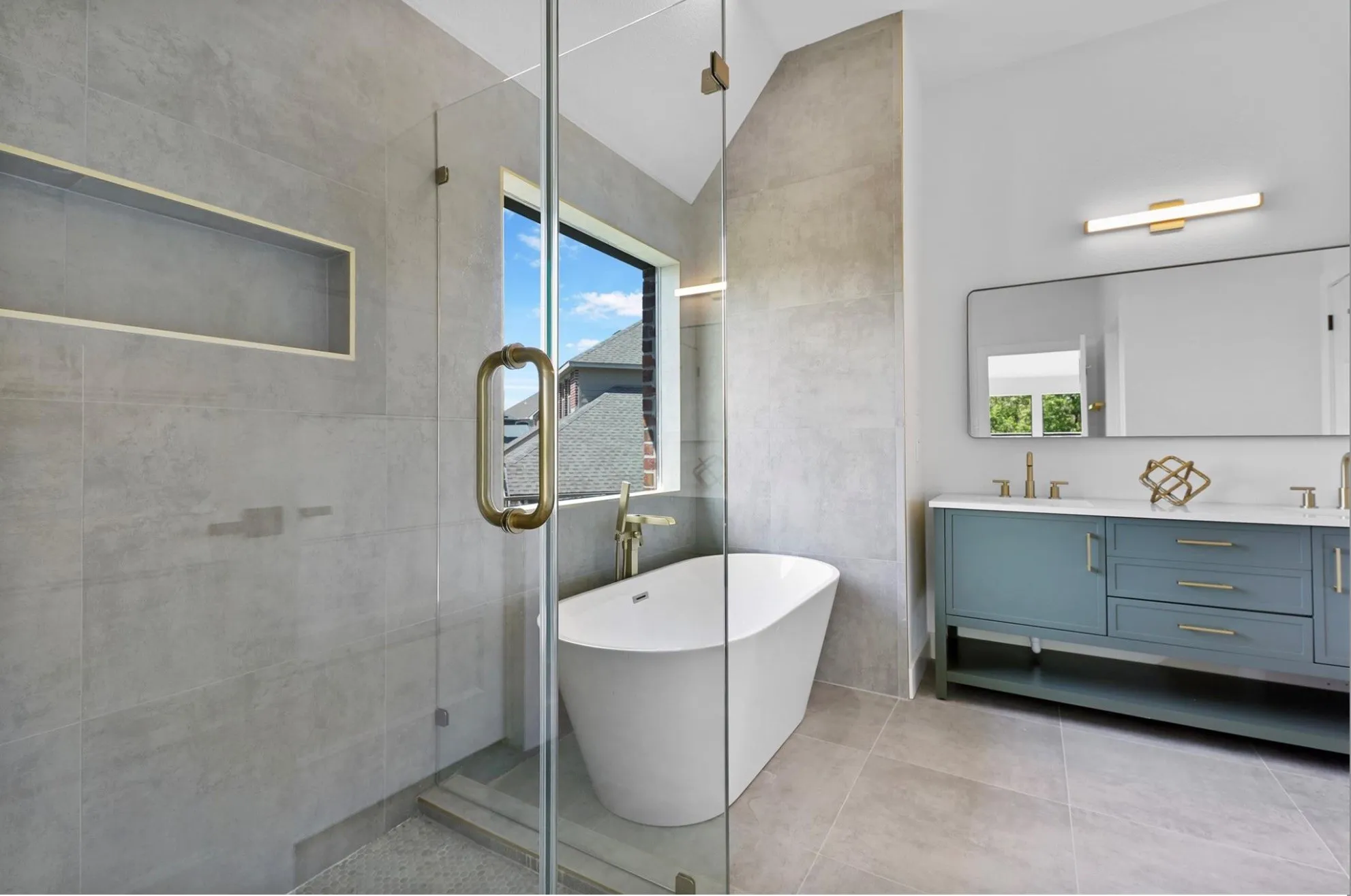 Glass-enclosed shower with a built-in niche, freestanding bathtub, dual vanity with white countertop, and gold-finish fixtures