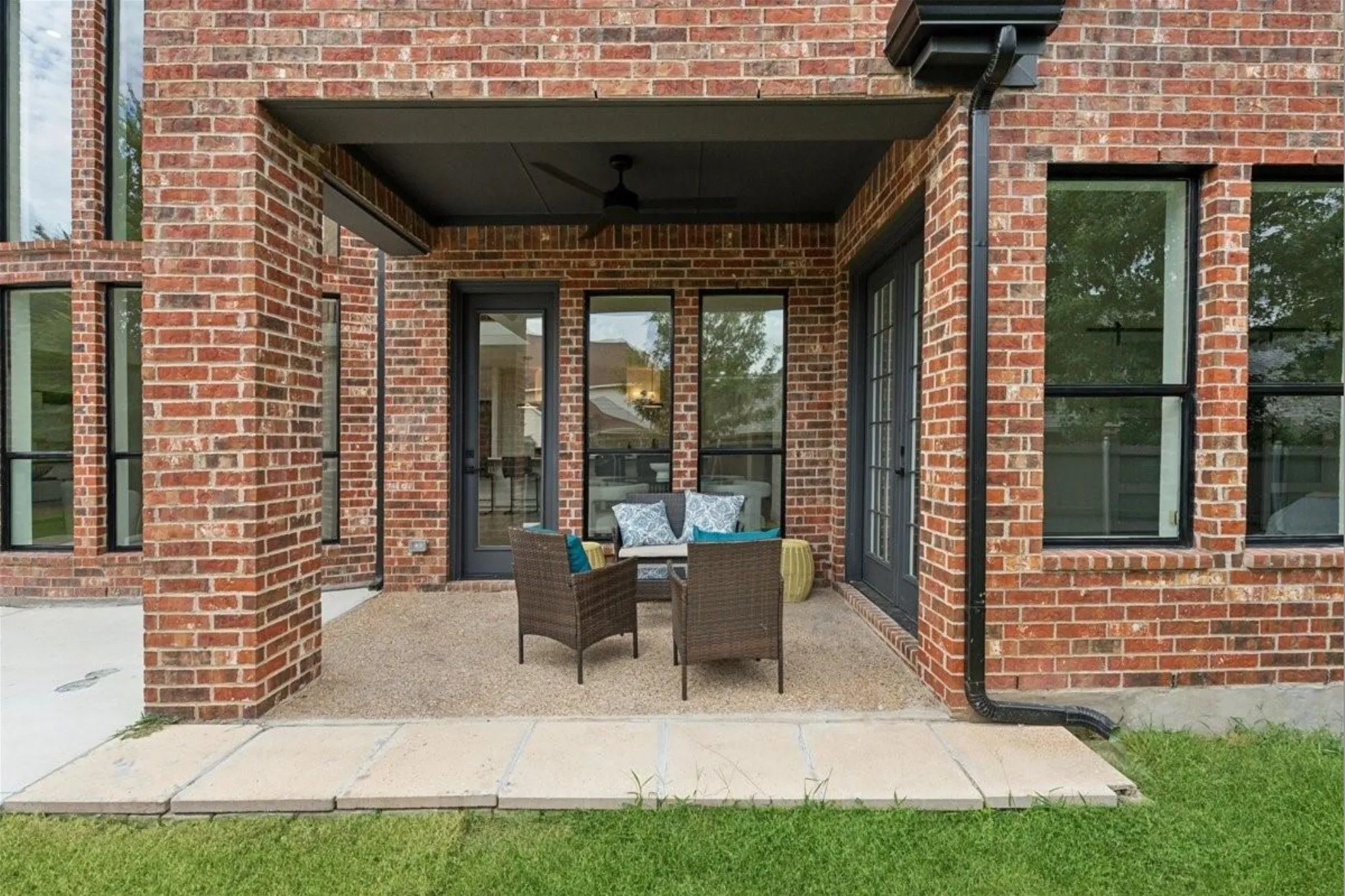 Covered outdoor patio with a ceiling fan, brick exterior, and multiple large windows