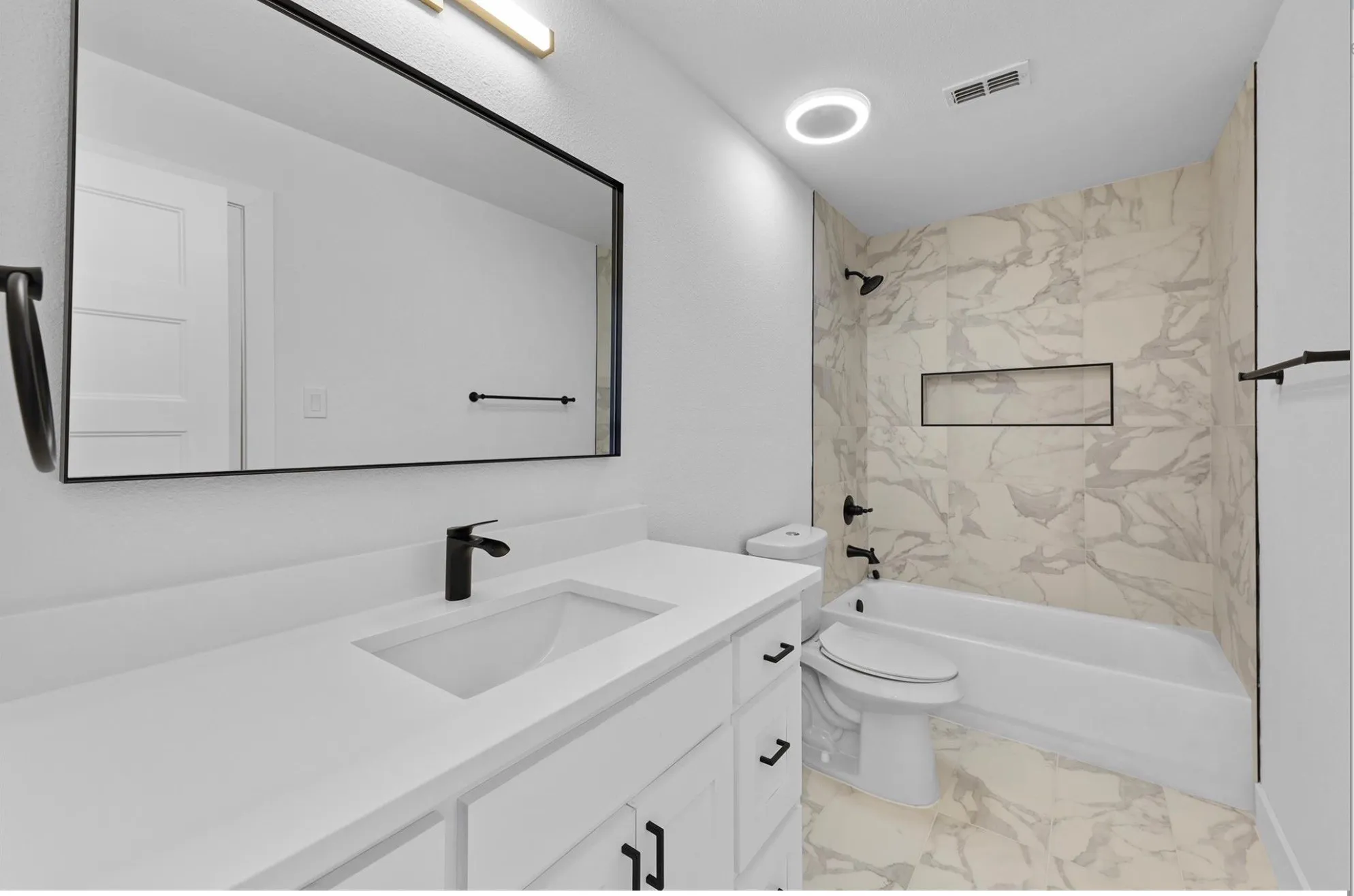 Contemporary bathroom featuring a vanity with an integrated sink, matte black fixtures, a rectangular framed mirror, and a tiled tub surround with an integrated niche