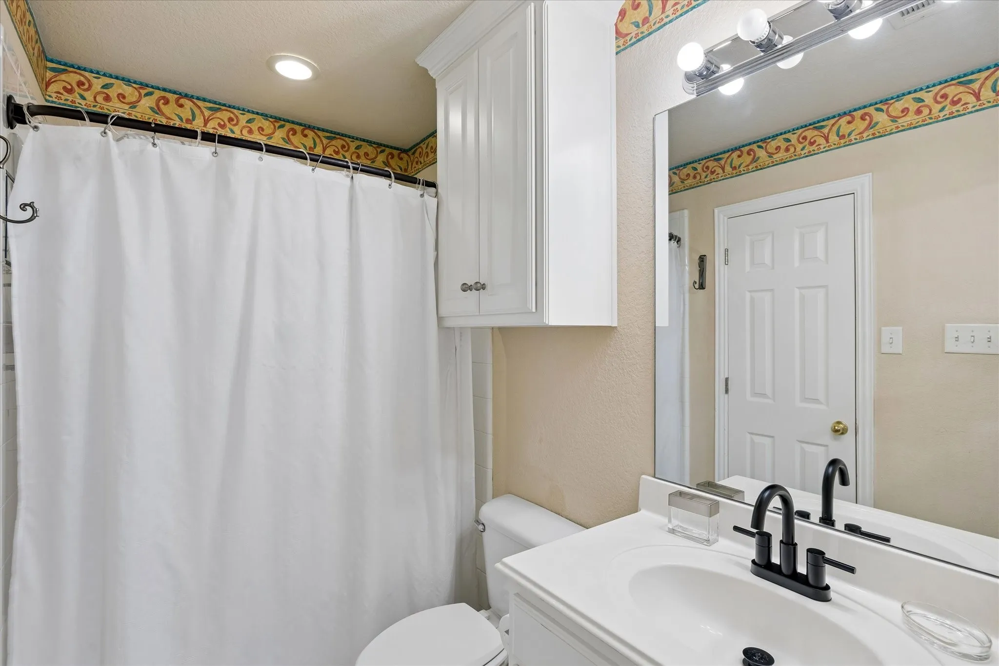 White vanity with integrated sink, matte black faucet, wall-mounted mirror, and overhead vanity lighting