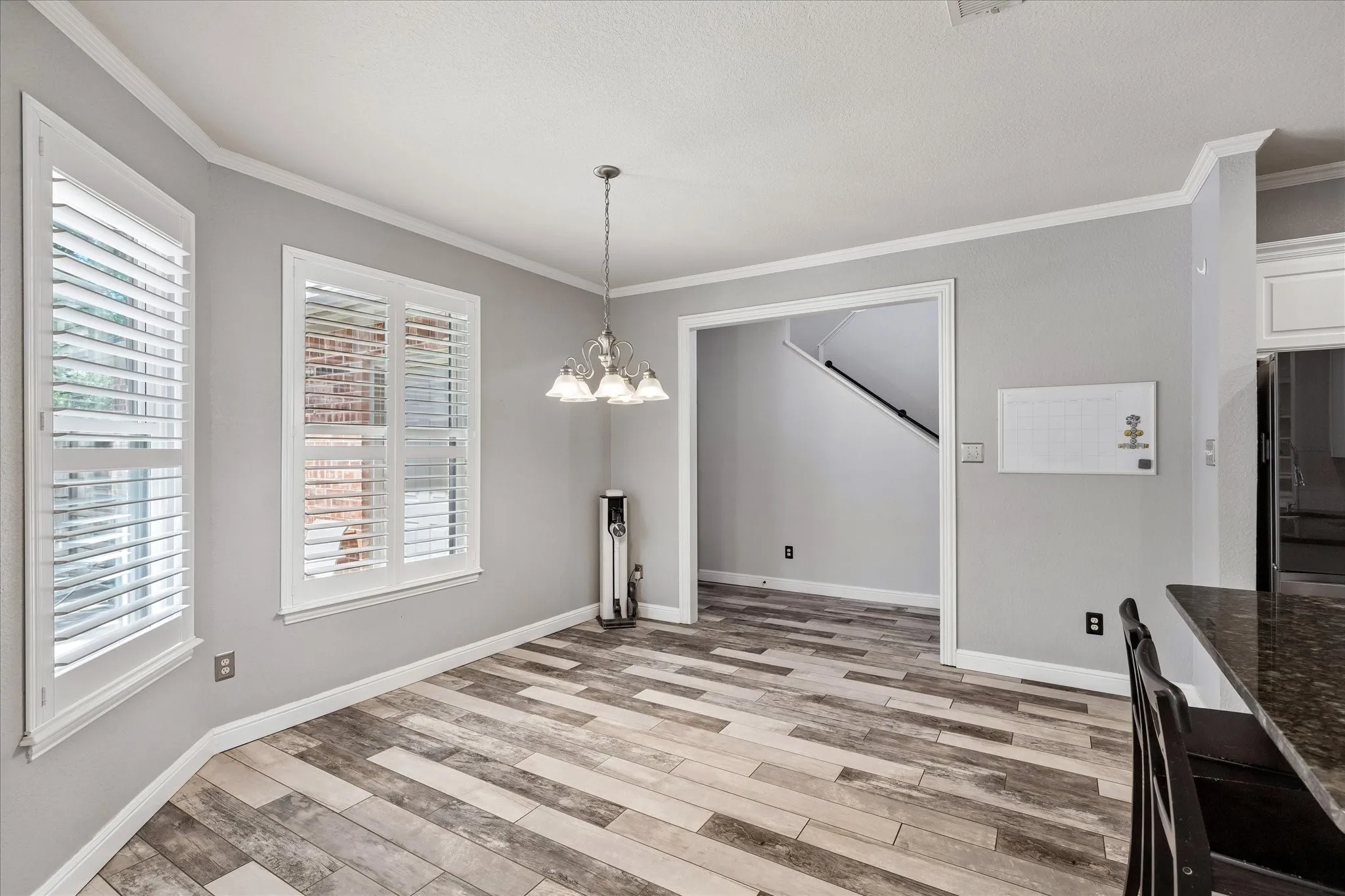 Wood-finish flooring, white plantation shutters, crown molding, and a chandelier illuminate this dining area