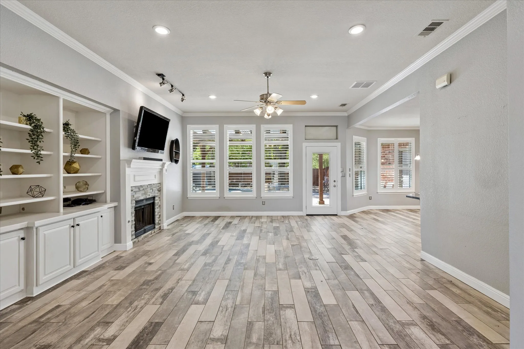 Spacious living area featuring wood-finish flooring, a built-in shelving unit, and a stone-clad fireplace