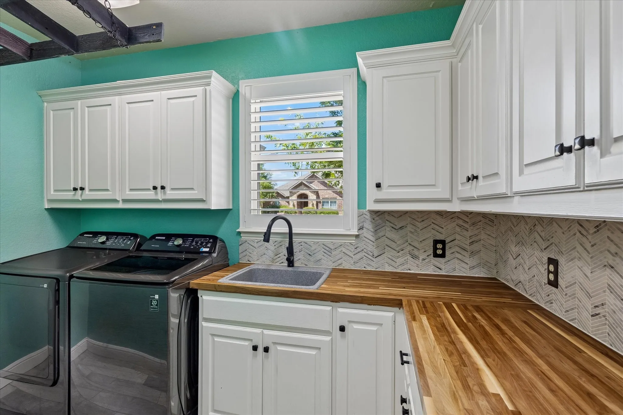 White shaker-style cabinetry, wood-finish countertops, undermount sink with a matte black faucet, and chevron-patterned tile backsplash