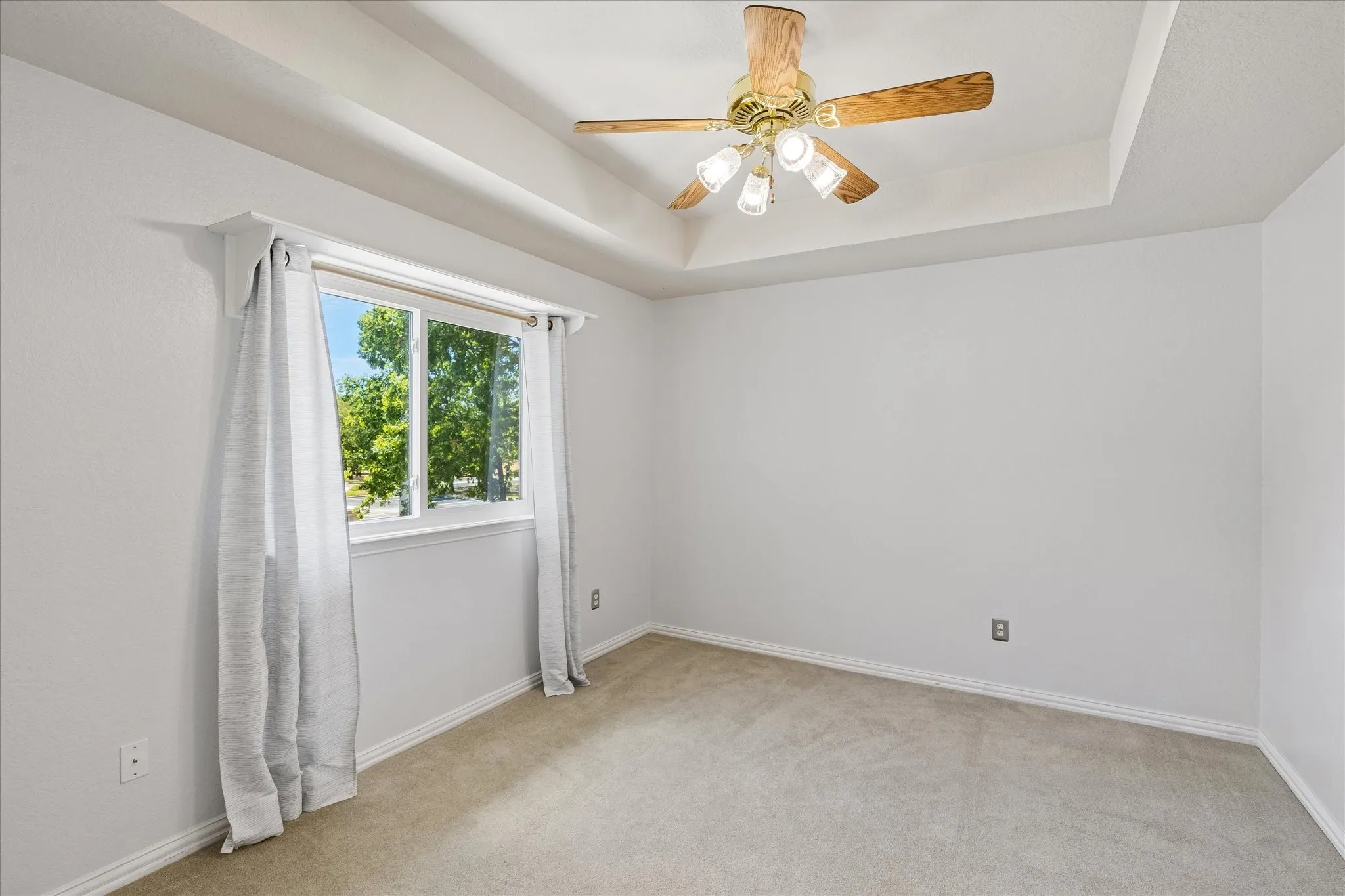 Tray ceiling with a ceiling fan, white walls, and a large window