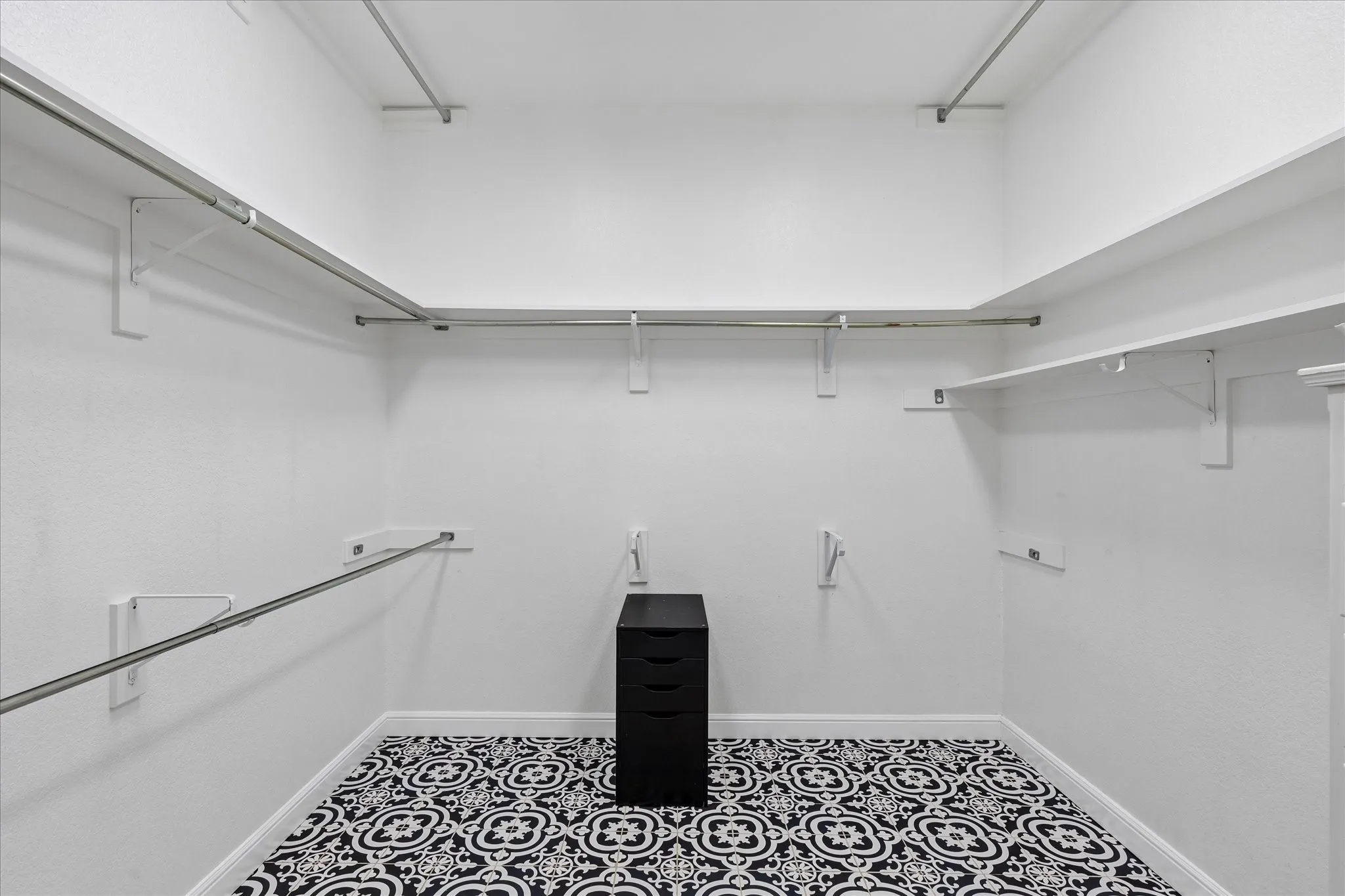 Spacious closet featuring patterned floor tiles, multiple clothing rods, and extensive shelving