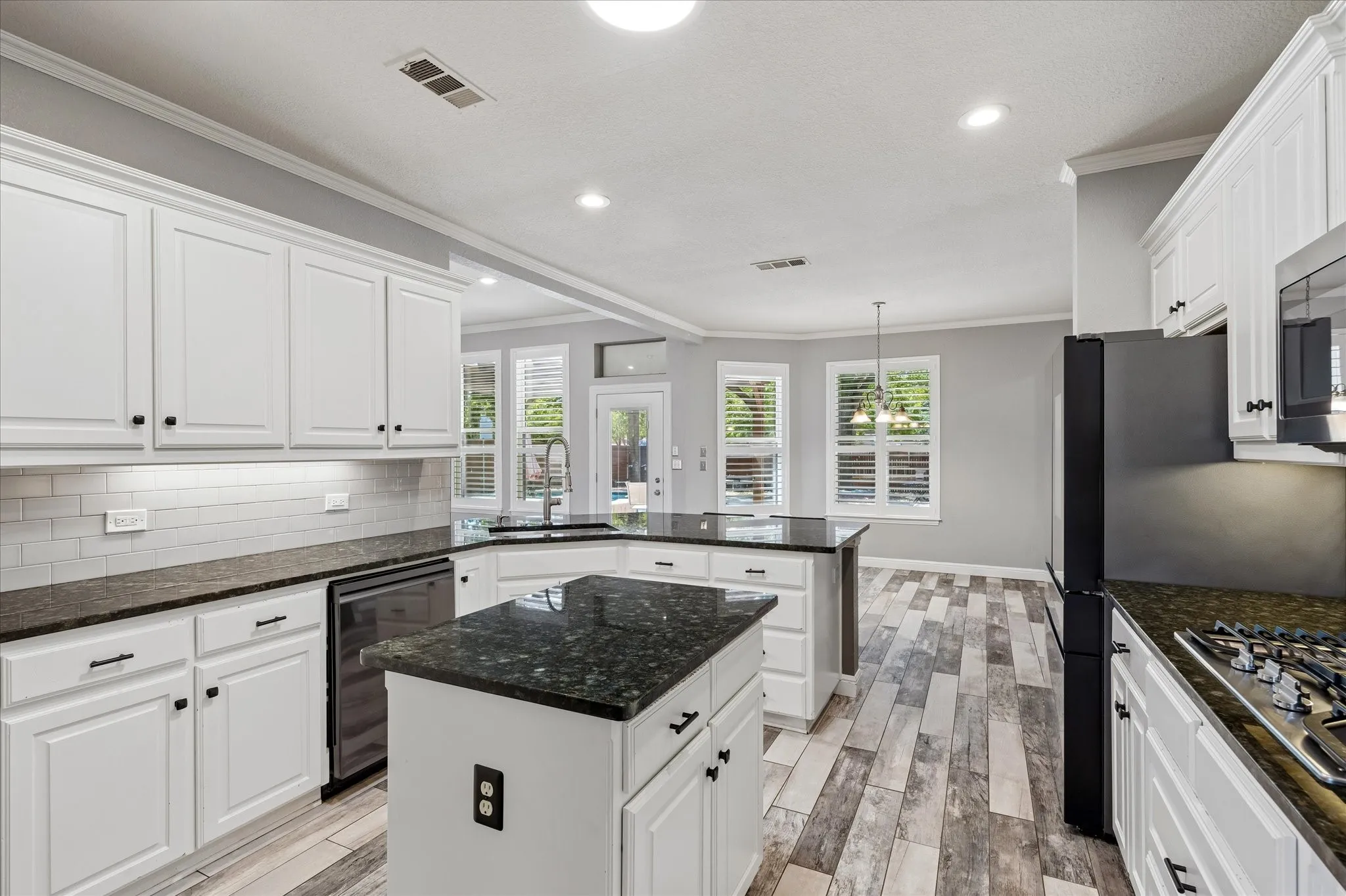 White cabinetry, dark stone countertops, wood-finish flooring, stainless steel appliances, and a subway tile backsplash