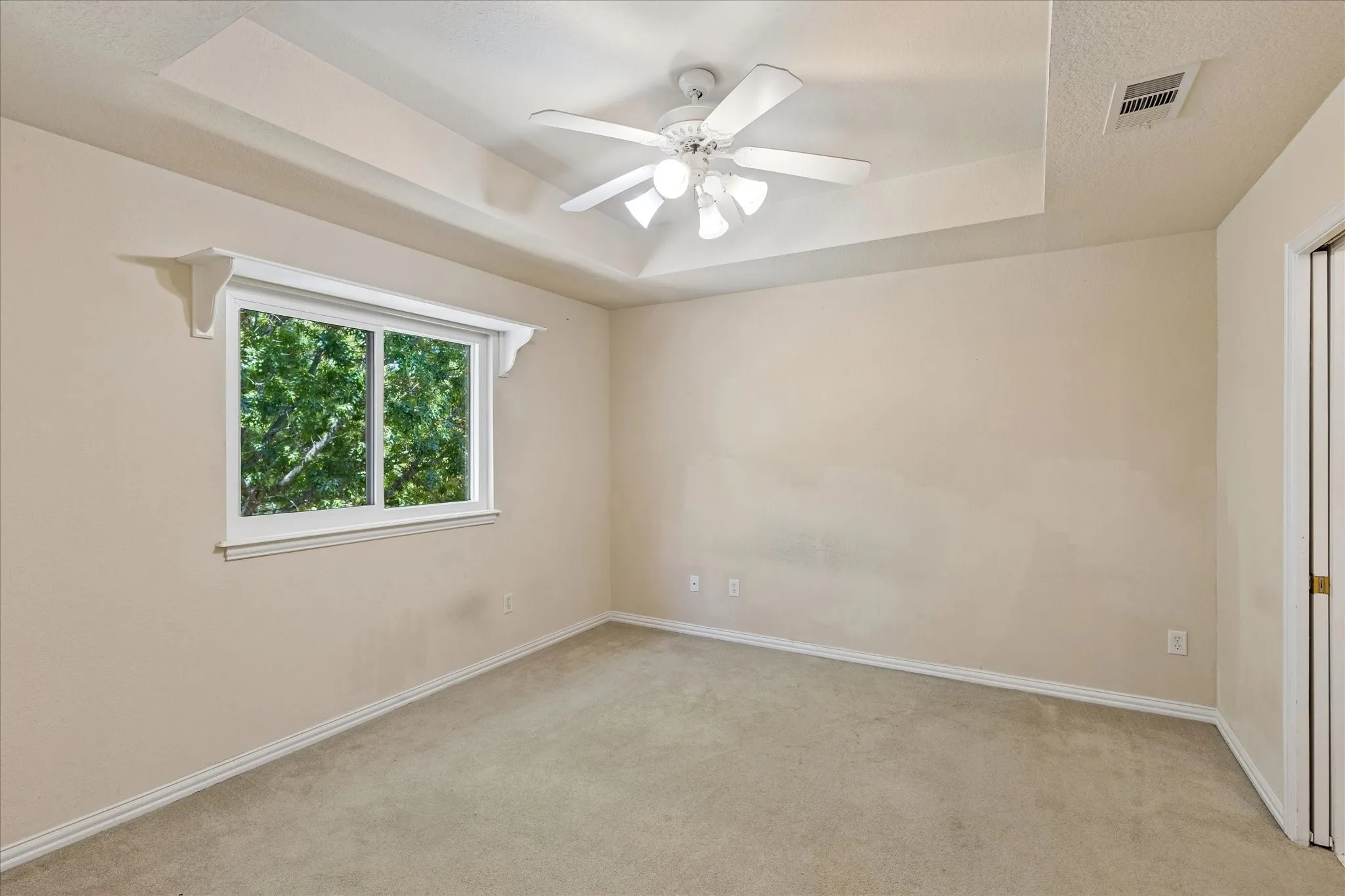 Recessed ceiling with a ceiling fan, carpeted flooring, and a double-pane window with decorative corbels