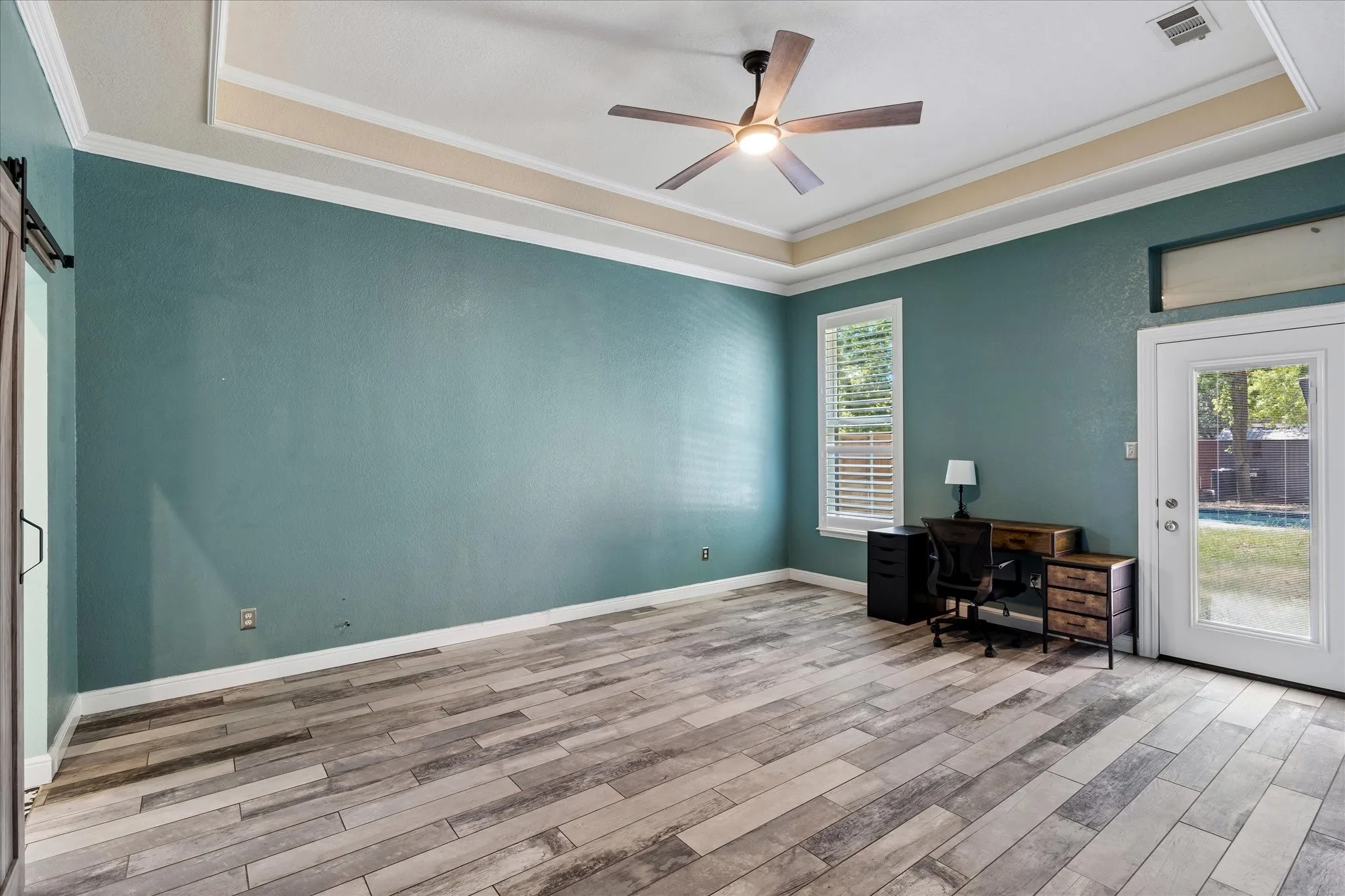 Tray ceiling with crown molding, wood-finish flooring, ceiling fan, natural light from exterior window, and glass-paneled exterior door