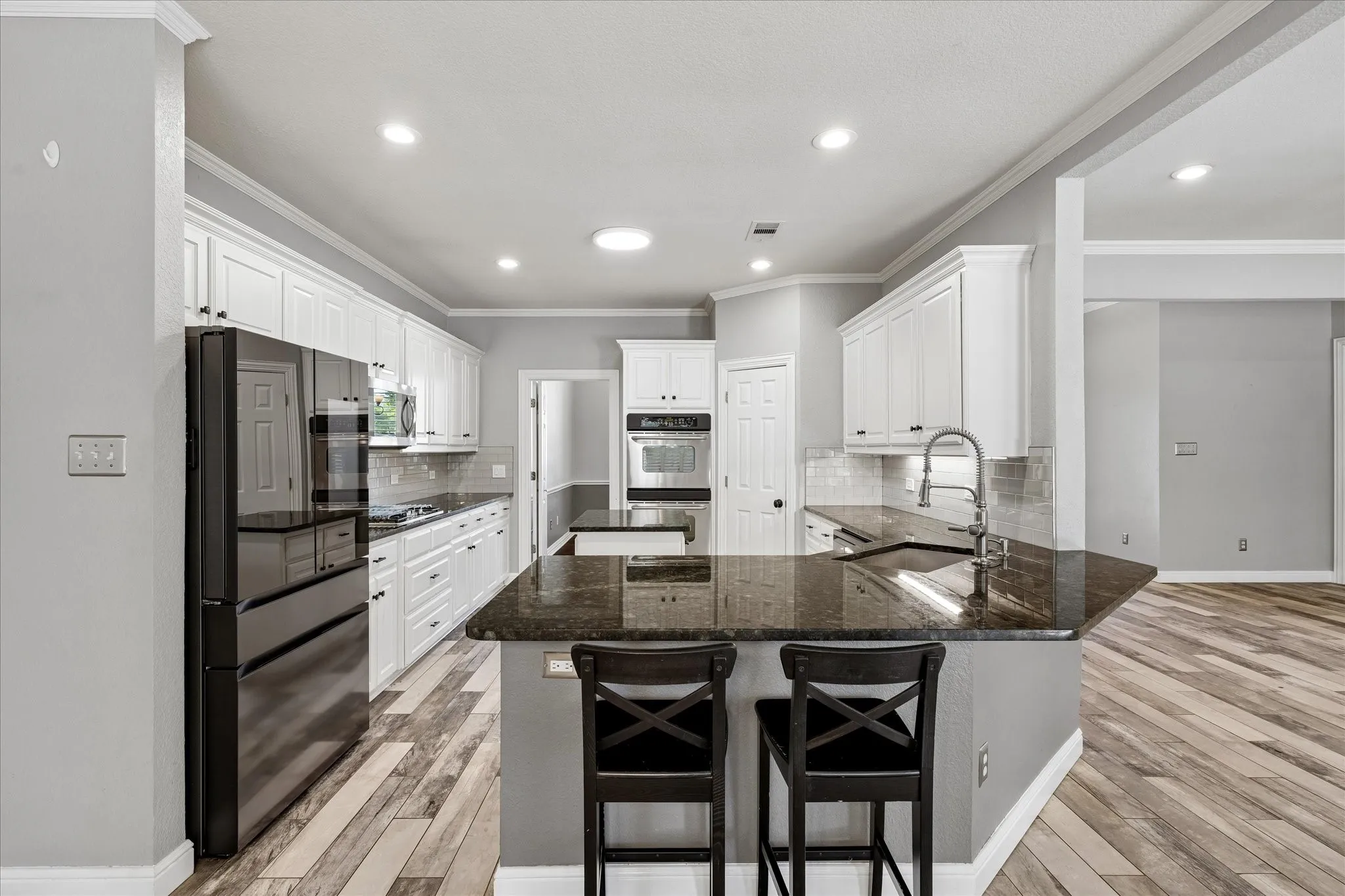 Kitchen featuring wood-finish flooring, white cabinetry, dark countertops, a built-in oven, and a kitchen island with a sink