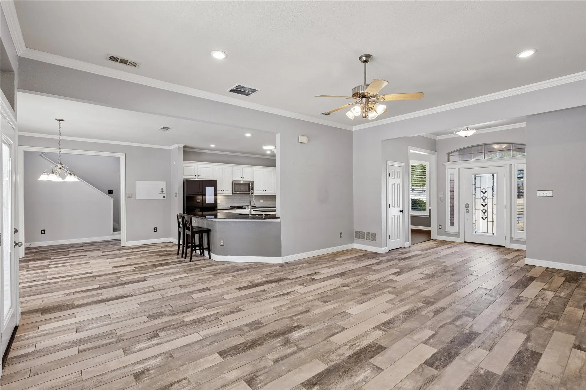 Wood-finish flooring throughout, kitchen with white cabinetry and stainless steel appliances, recessed lighting, ceiling fan, and decorative glass entry door with sidelights