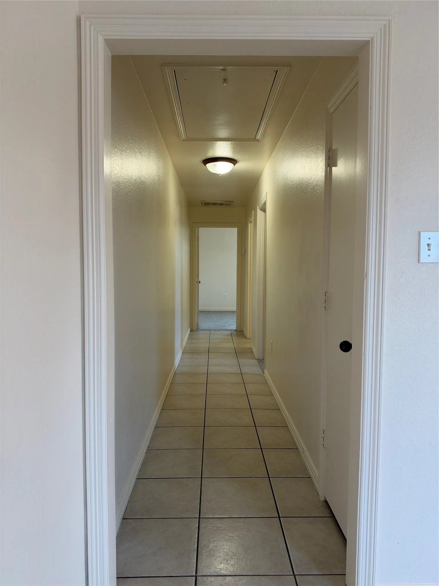 Hallway with square tile flooring, flush mount lighting, and white trim