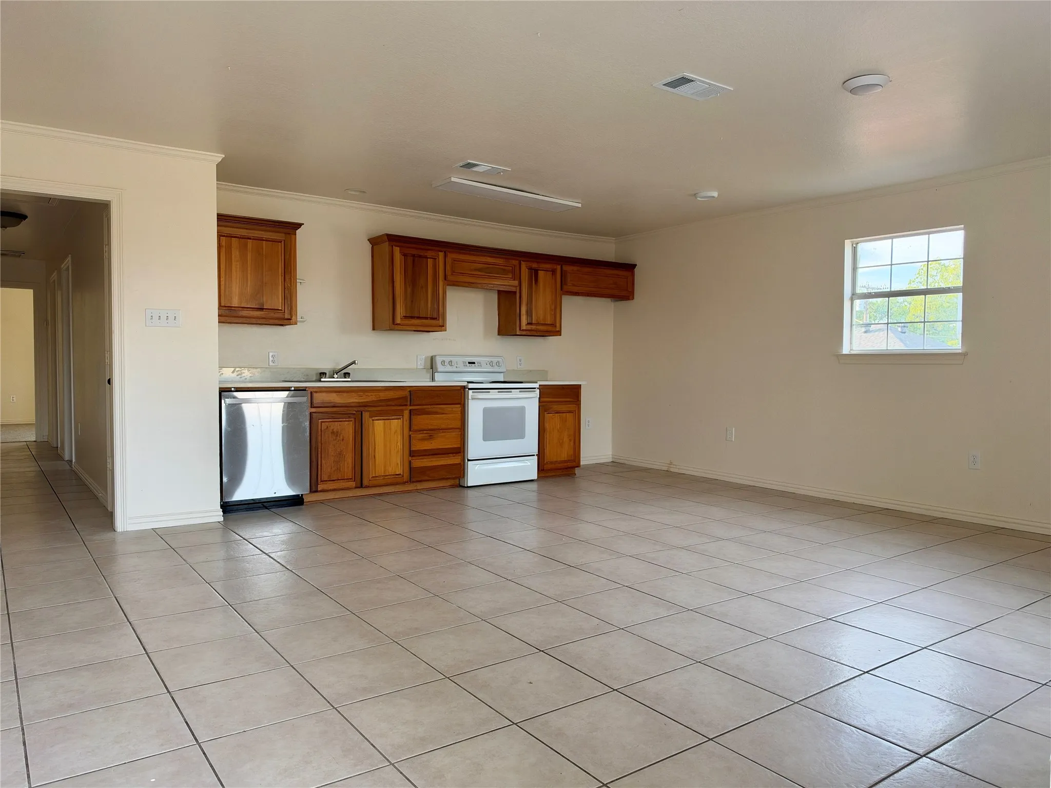Open-concept living area with tiled flooring, a kitchen featuring wood cabinetry, a stainless steel dishwasher, and a white electric range