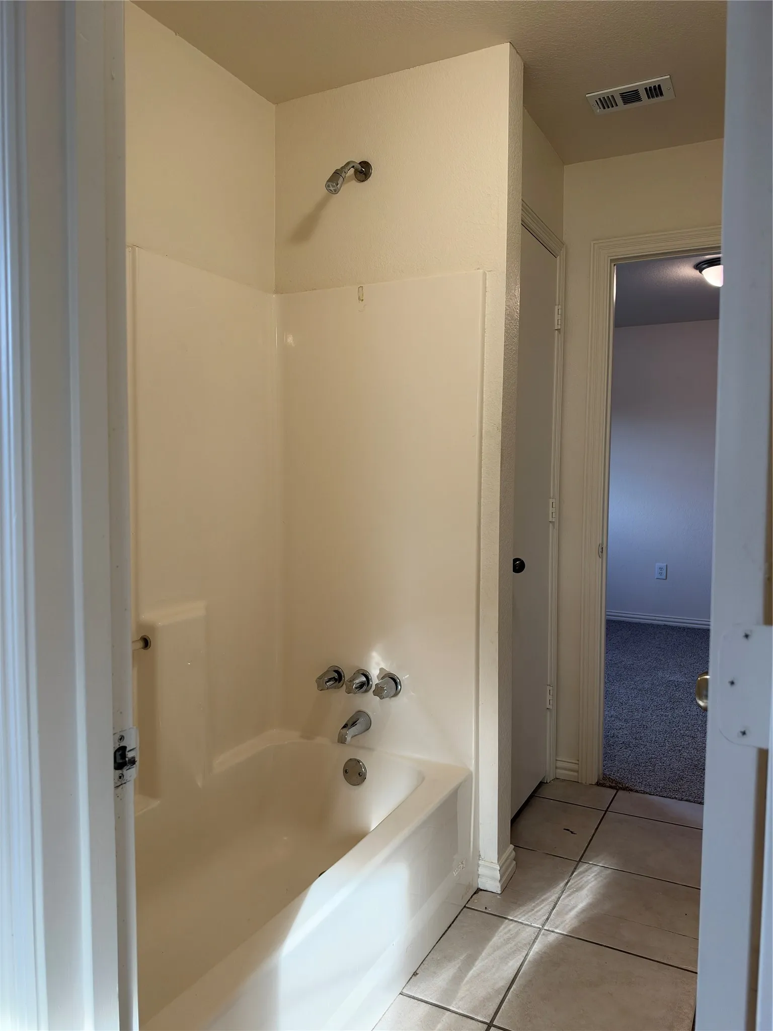 Bathtub with integrated shower surround, chrome fixtures, and tiled flooring