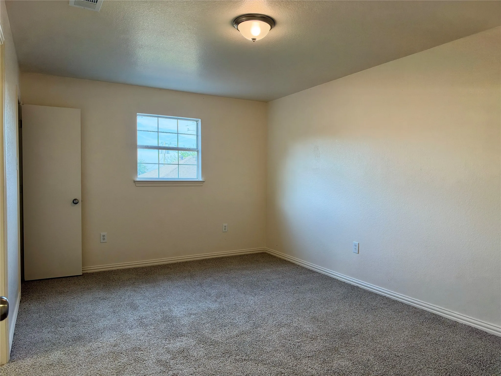 Neutral tone wall finish with a single window featuring grid panes and a flush-mount ceiling light fixture