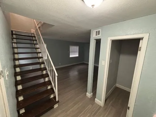 Wood-finish flooring throughout, a staircase with white metal railings and dark wood treads, and a built-in closet space