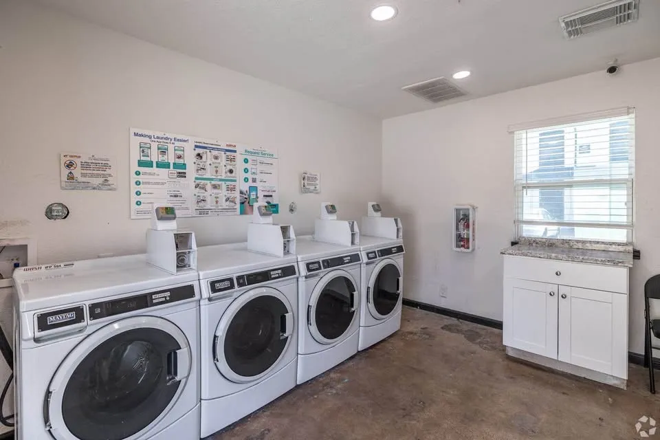 On-site laundry facility featuring multiple front-loading washers and dryers, a built-in cabinet with a stone-finish countertop, and recessed lighting