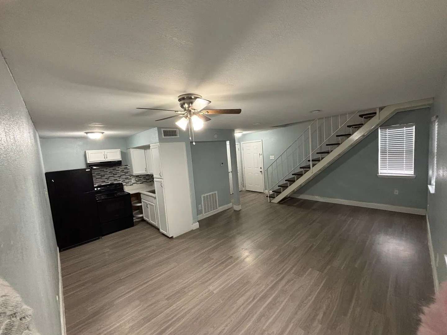 Open concept living area featuring wood-finish flooring, a ceiling fan, and a kitchen with white cabinetry and a patterned tile backsplash